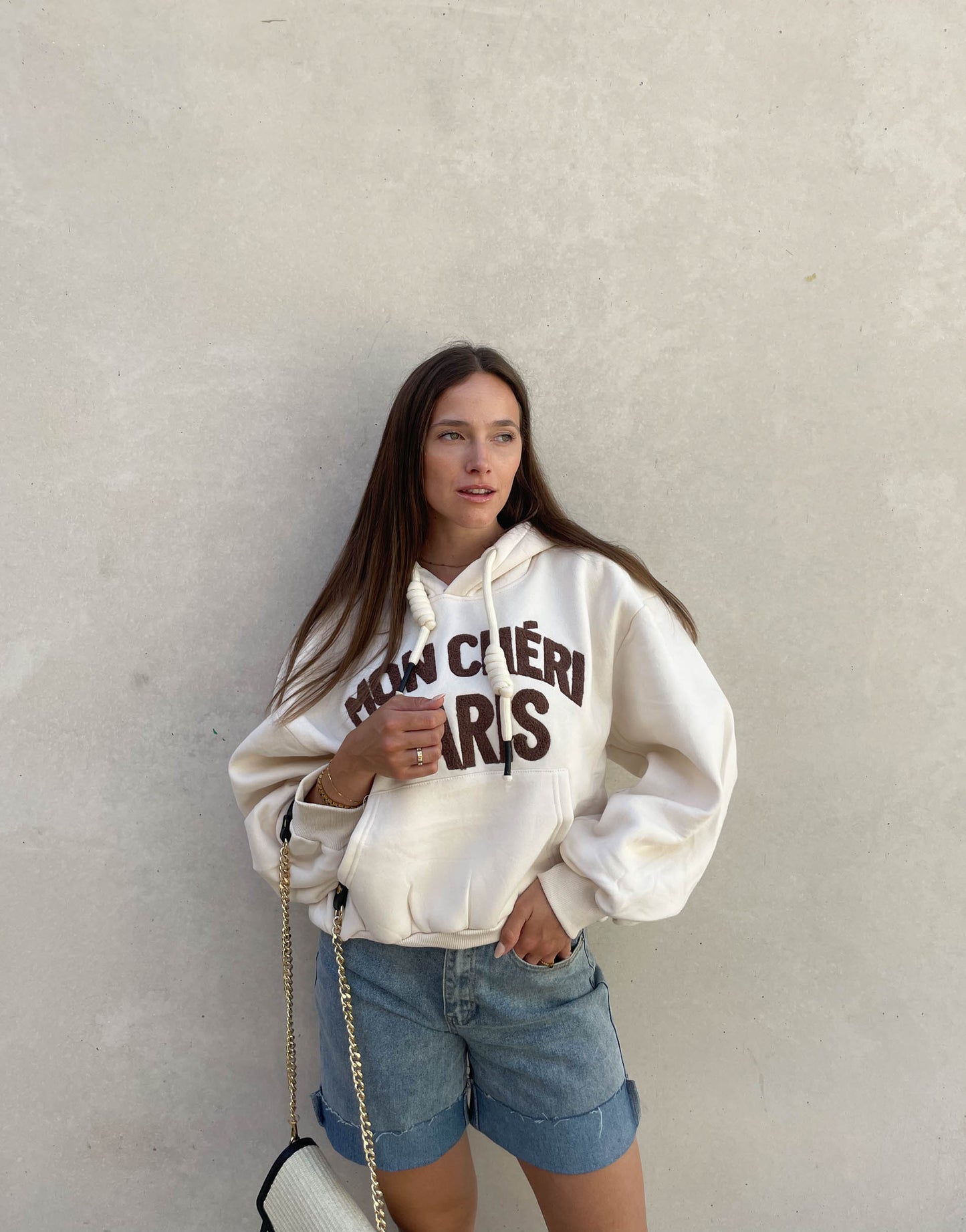 Frau mit brauen Haaren trägt oversize Hoodie mit Aufschrift in Beige