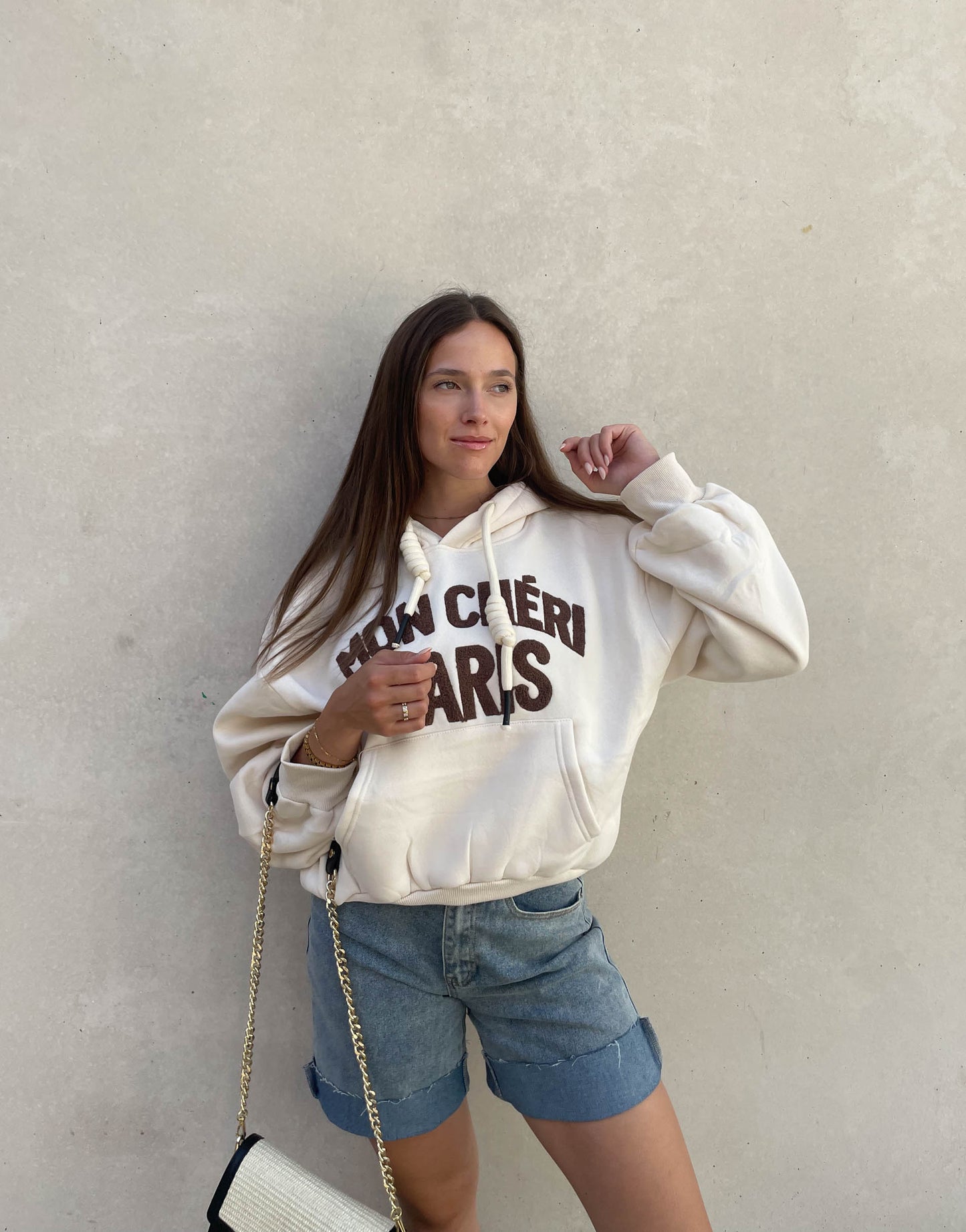 Frau mit brauen Haaren trägt oversize Hoodie mit Aufschrift in Beige