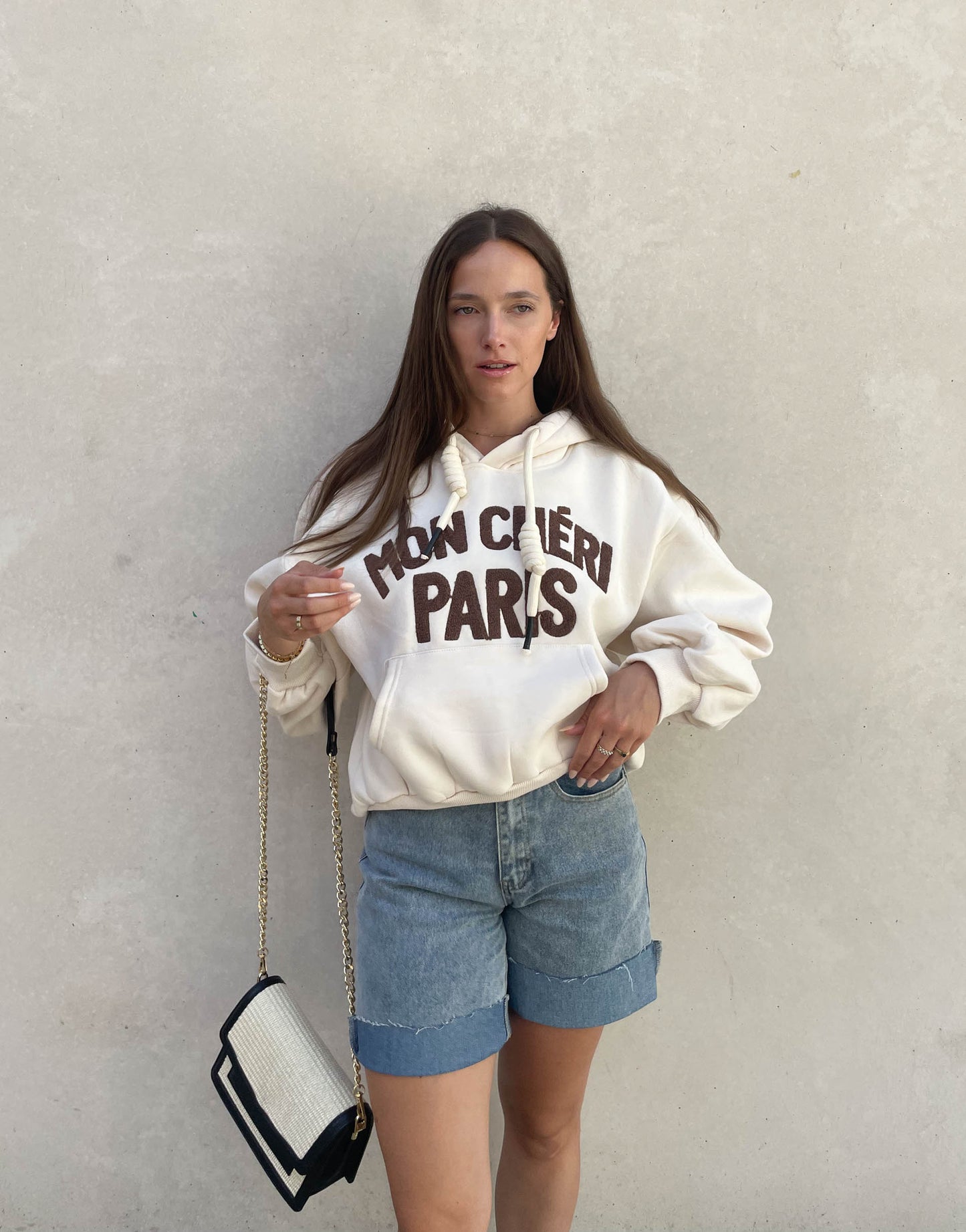 Frau mit brauen Haaren trägt oversize Hoodie mit Aufschrift in Beige