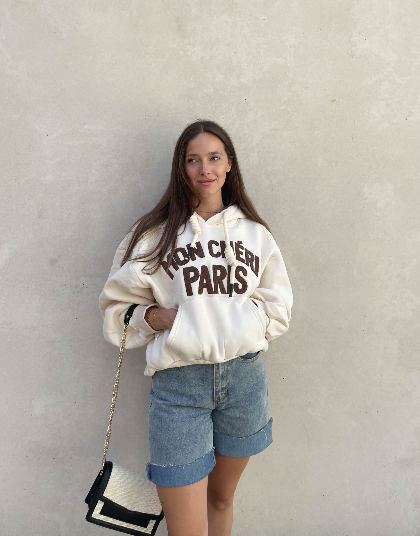 Frau mit brauen Haaren trägt oversize Hoodie mit Aufschrift in Beige