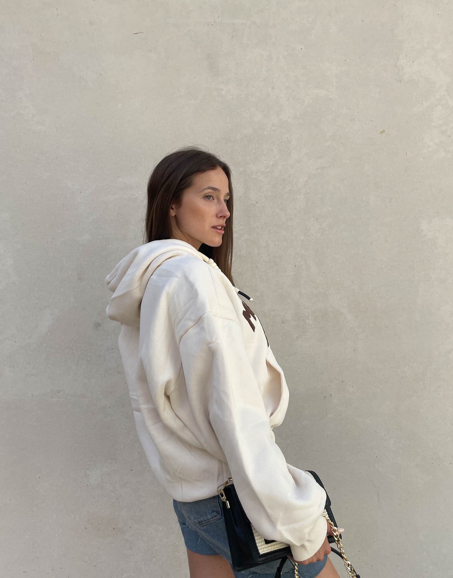 Frau mit brauen Haaren trägt oversize Hoodie mit Aufschrift in Beige