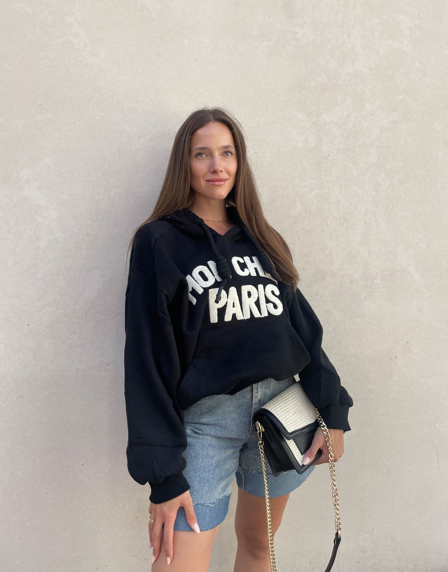 Frau mit brauen Haaren trägt oversize Hoodie mit Aufschrift in Schwarz
