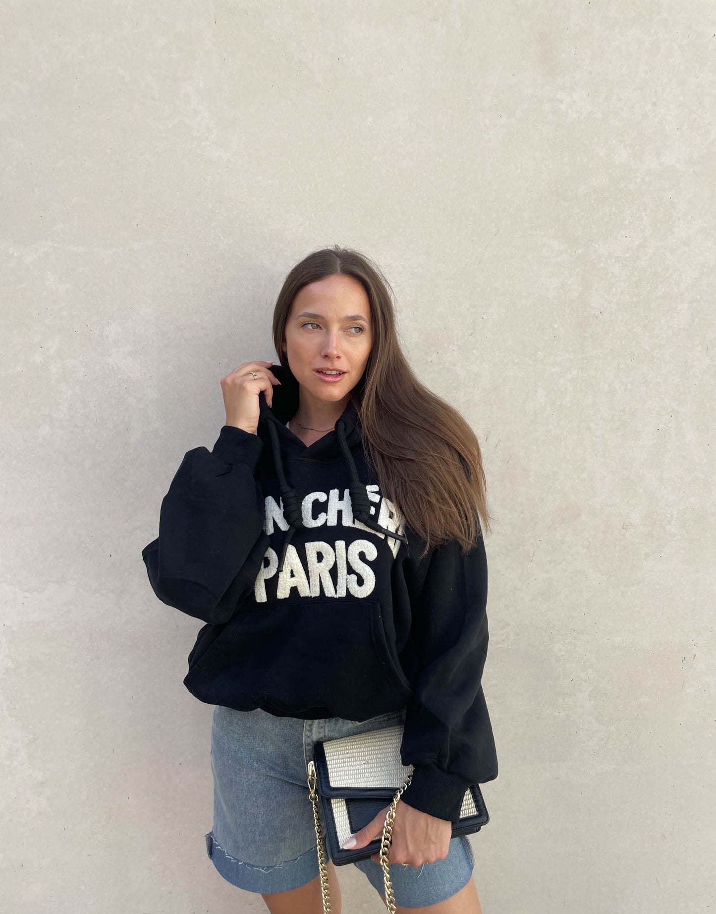 Frau mit brauen Haaren trägt oversize Hoodie mit Aufschrift in Schwarz