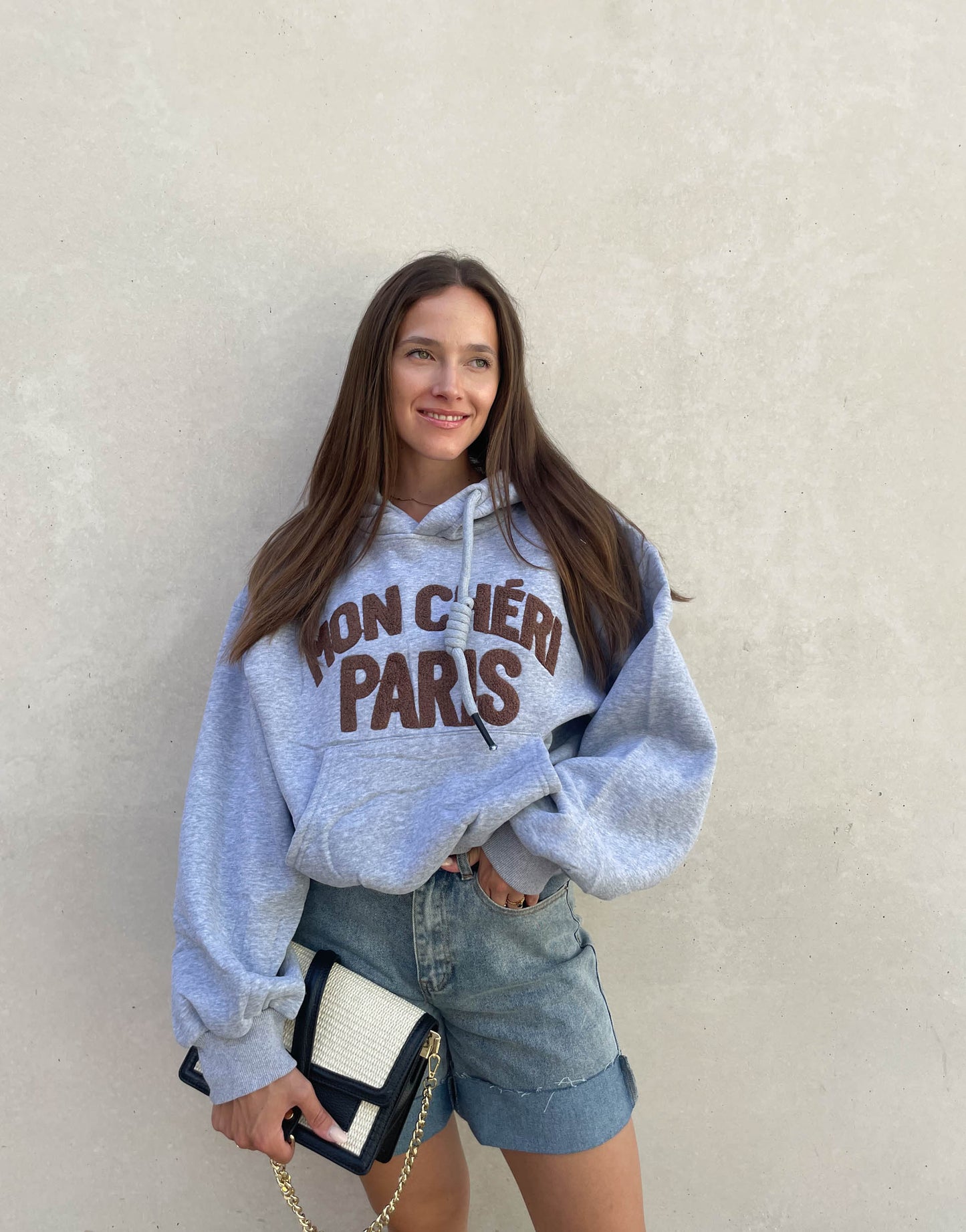 Frau mit brauen Haaren trägt oversize Hoodie mit Aufschrift in Grau
