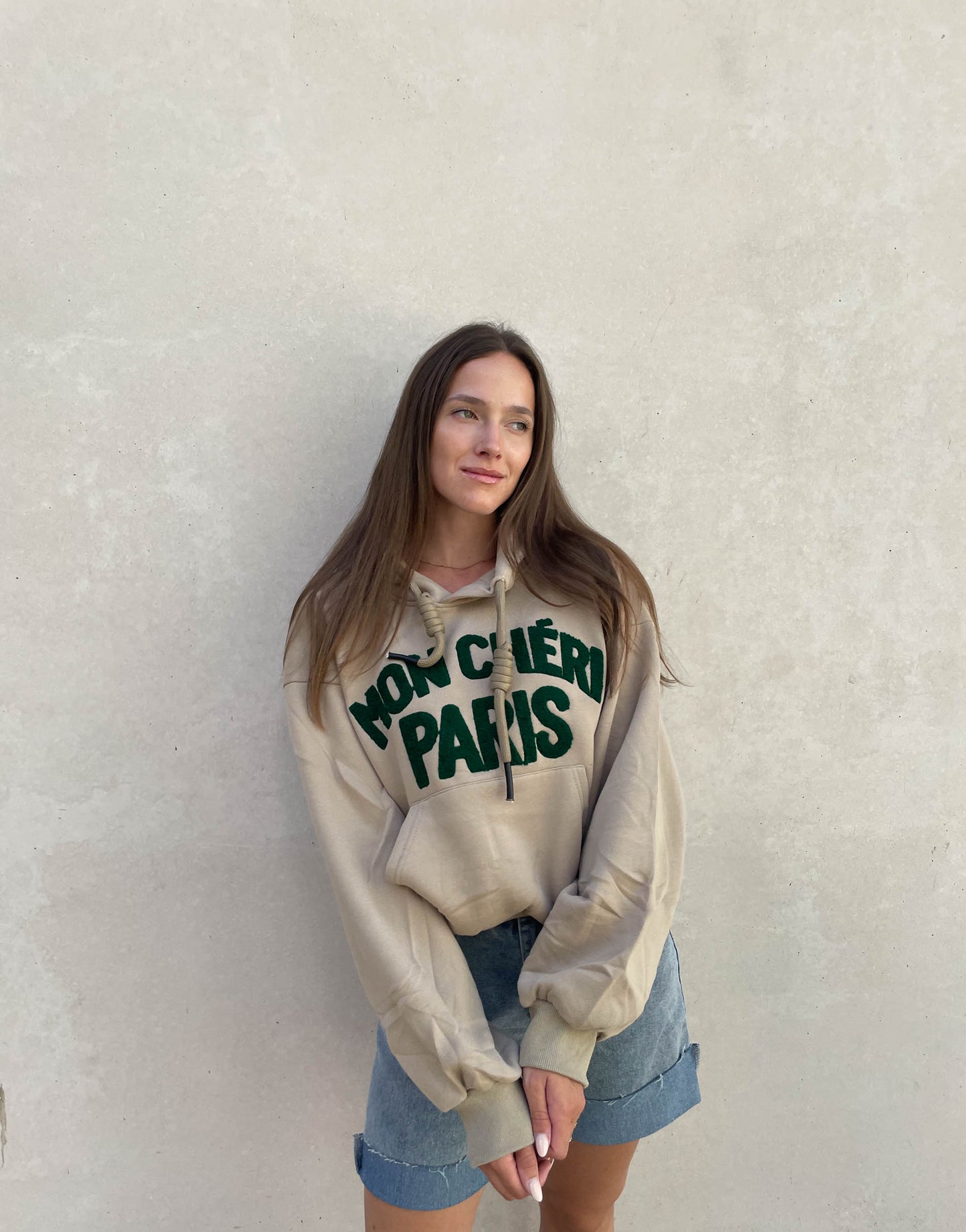 Frau mit brauen Haaren trägt oversize Hoodie mit Aufschrift in Taupe