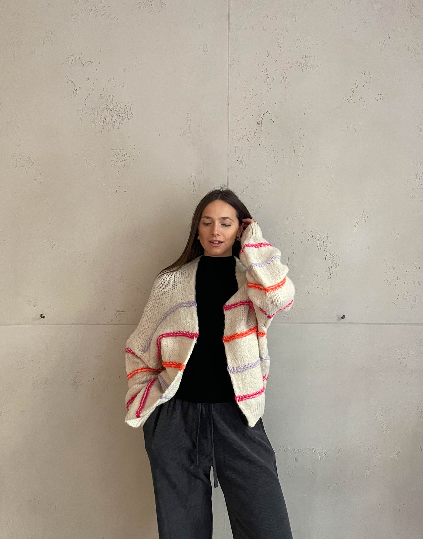 Frau mit brauen Haaren trägt Strickjacke mit Neon Aussennähten inBeige