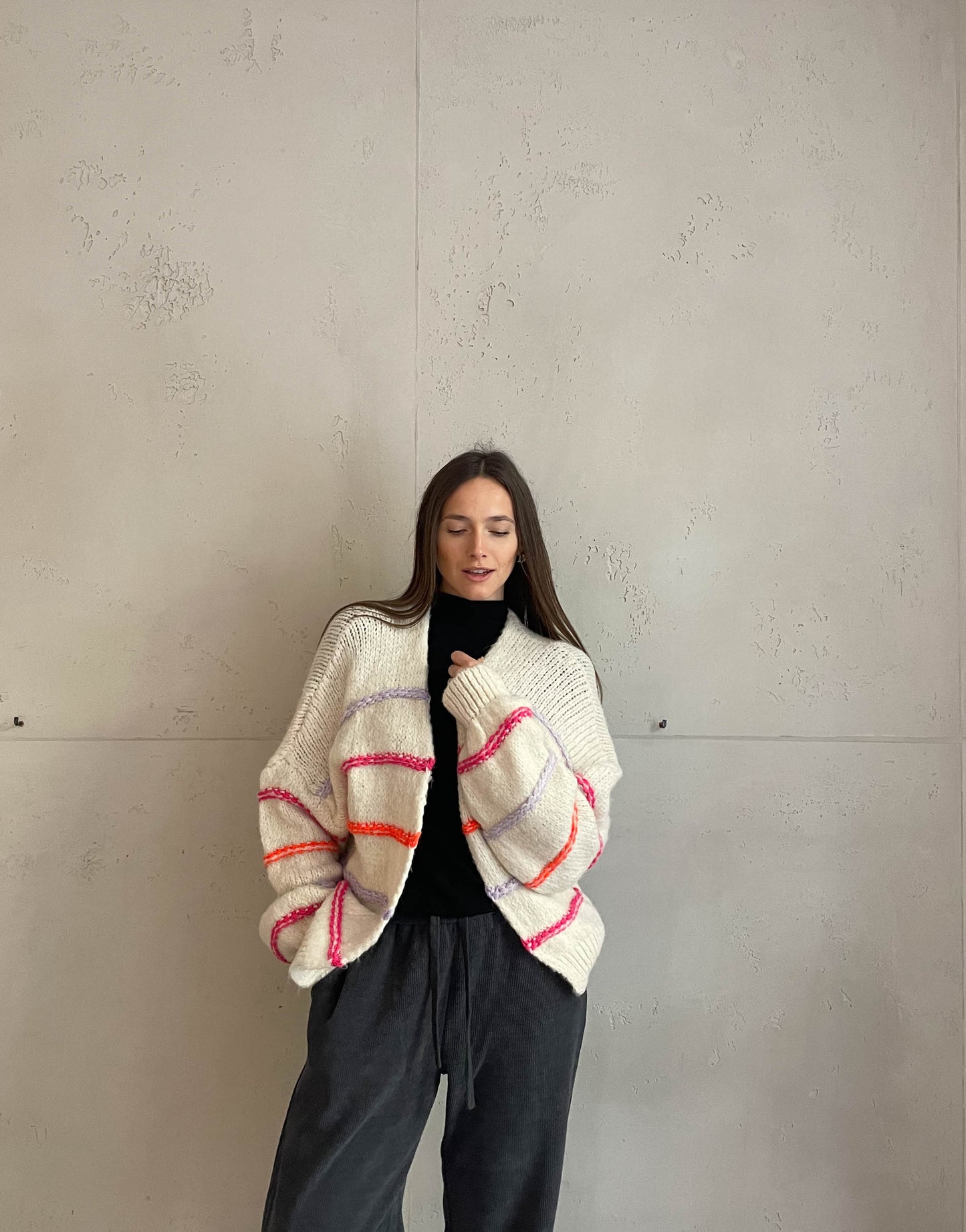 Frau mit brauen Haaren trägt Strickjacke mit Neon Aussennähten in Beige
