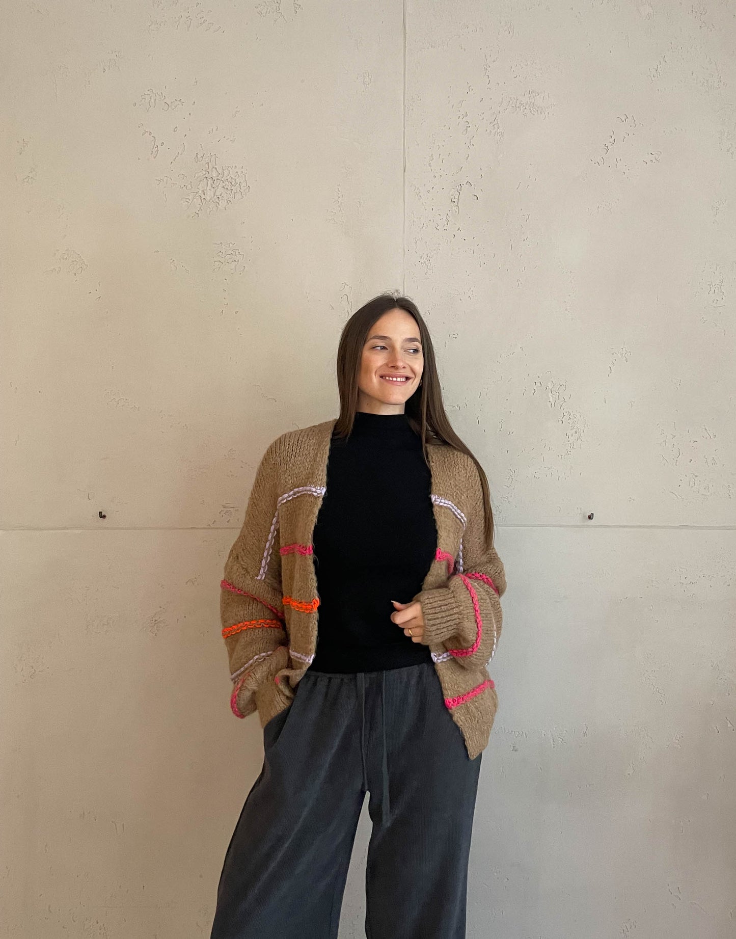 Frau mit brauen Haaren trägt Strickjacke mit Neon Aussennähten in Camel