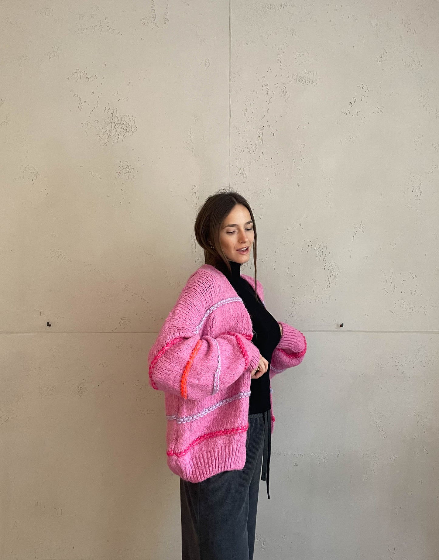 Frau mit brauen Haaren trägt Strickjacke mit Neon Aussennähten in Pink