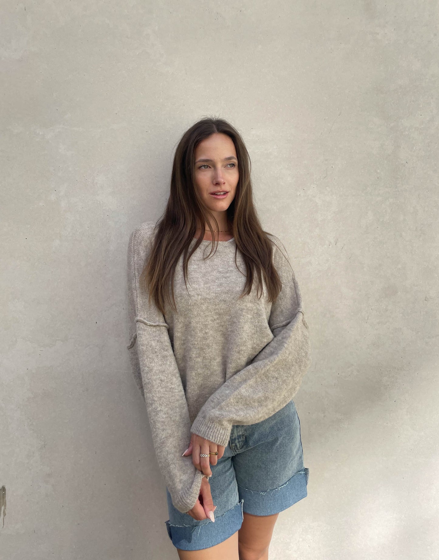 Frau mit brauen Haaren trägt Pullover mit Außennaht in Taupe 03