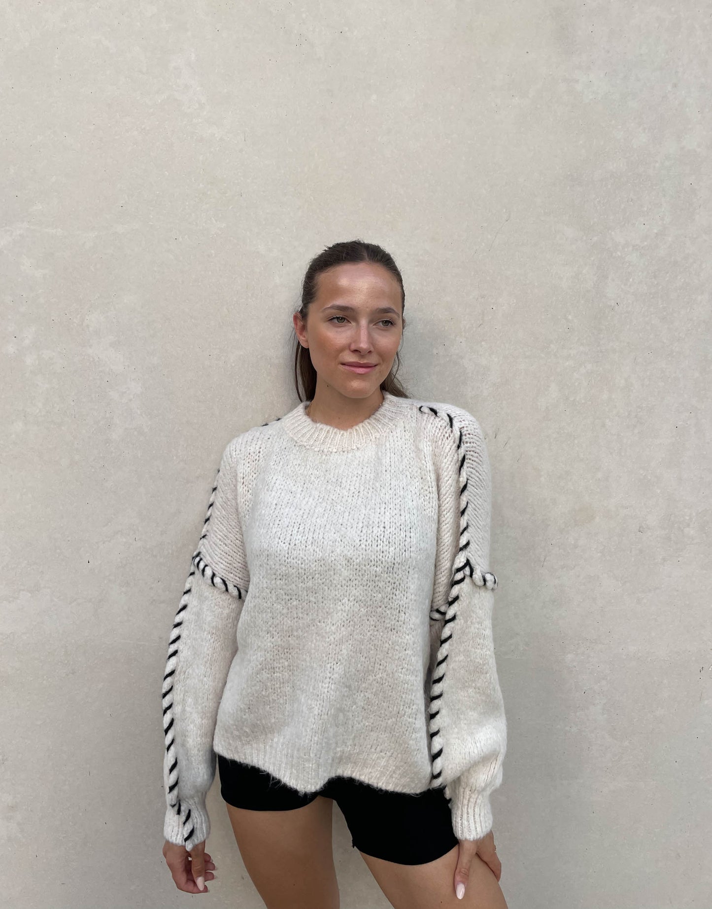 Frau mit brauen Haaren trägt Oversize Pullover in Wollweiß