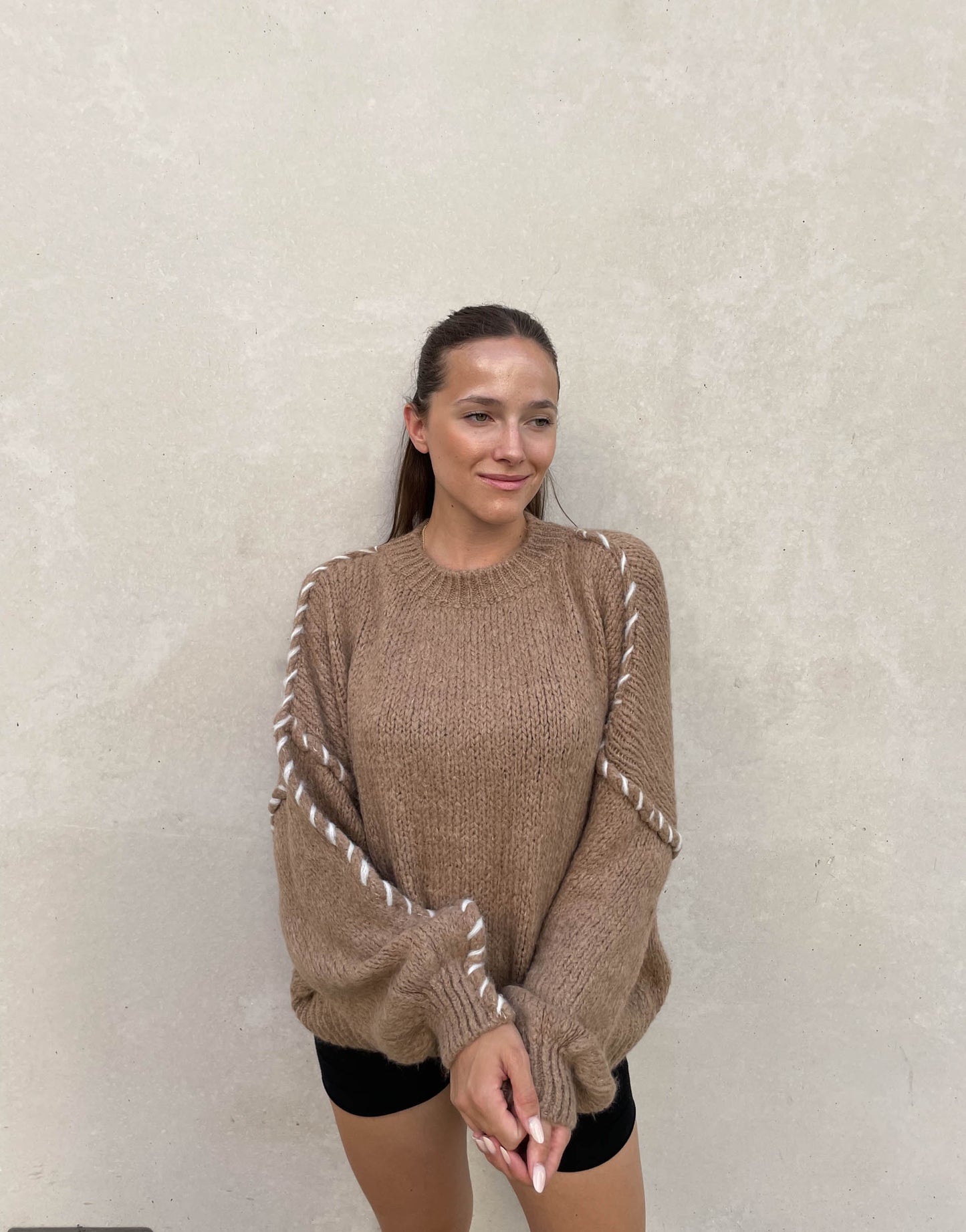 Frau mit brauen Haaren trägt Oversize Pullover in camel