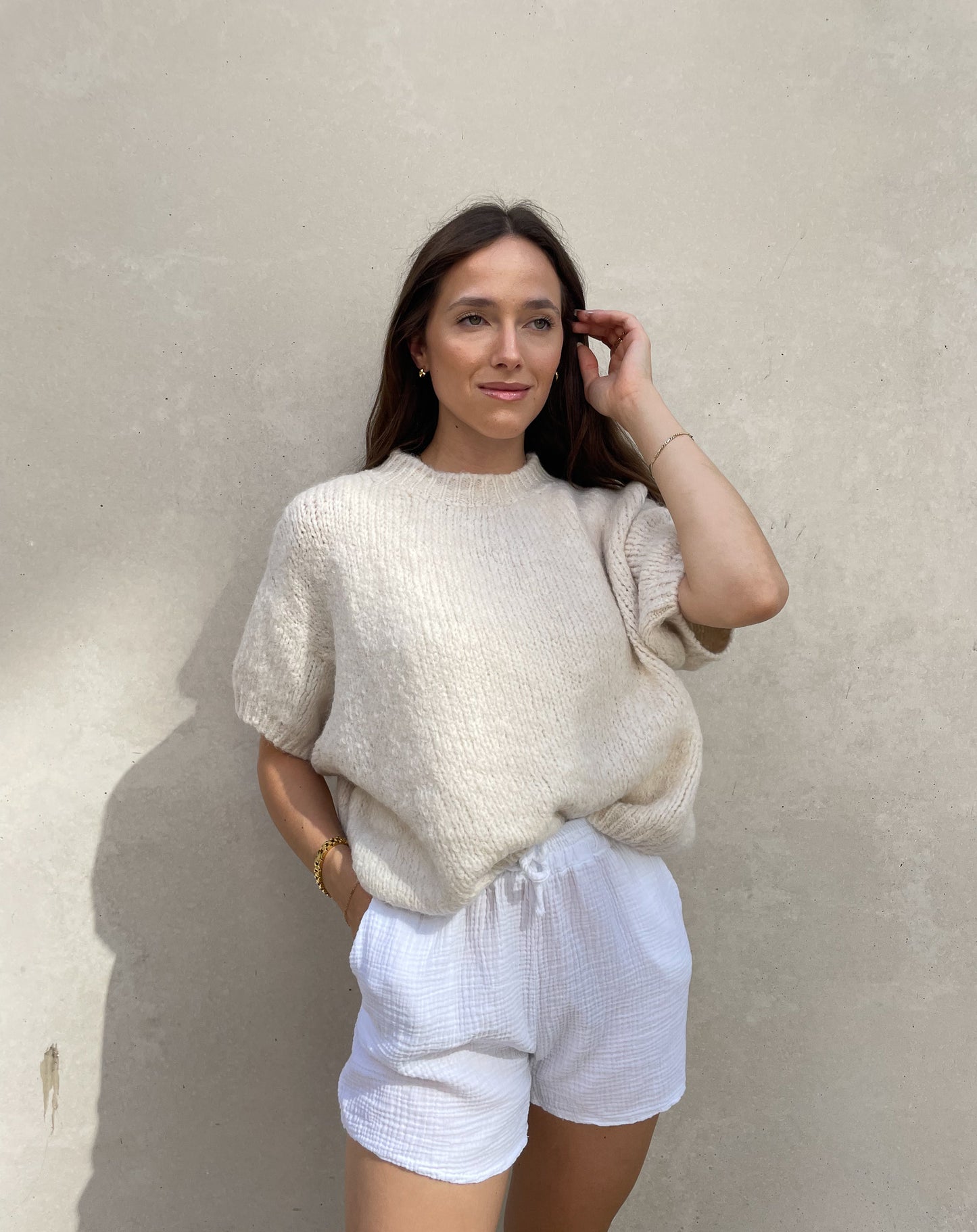 Frau mit brauen Haaren trägt Strickpullover mit Kurzarm in beige
