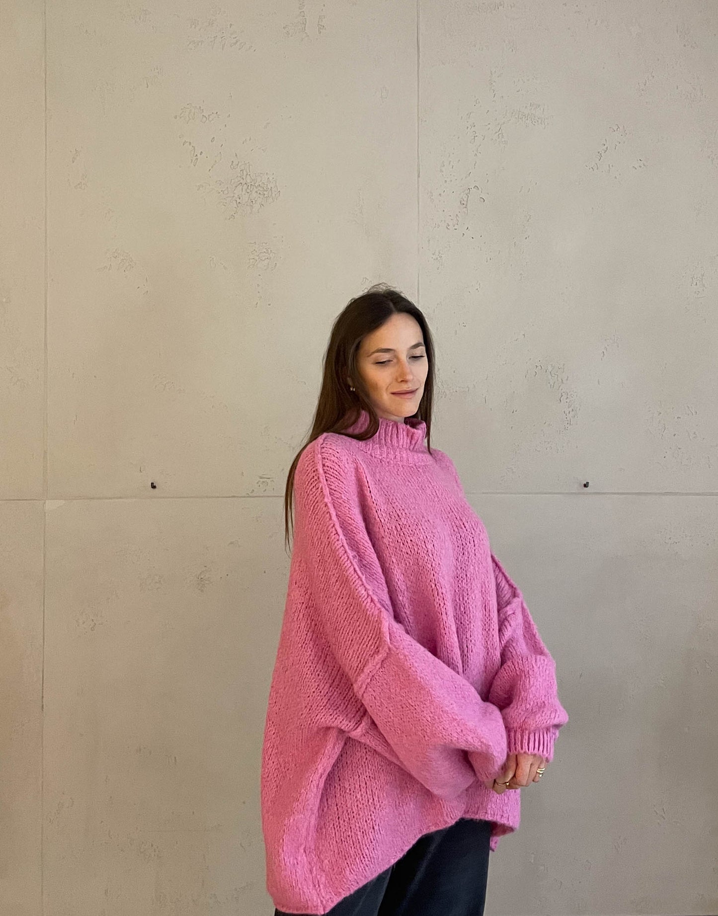 Frau mit brauen Haaren trägt oversize Pullover mit Stehkragen in pink