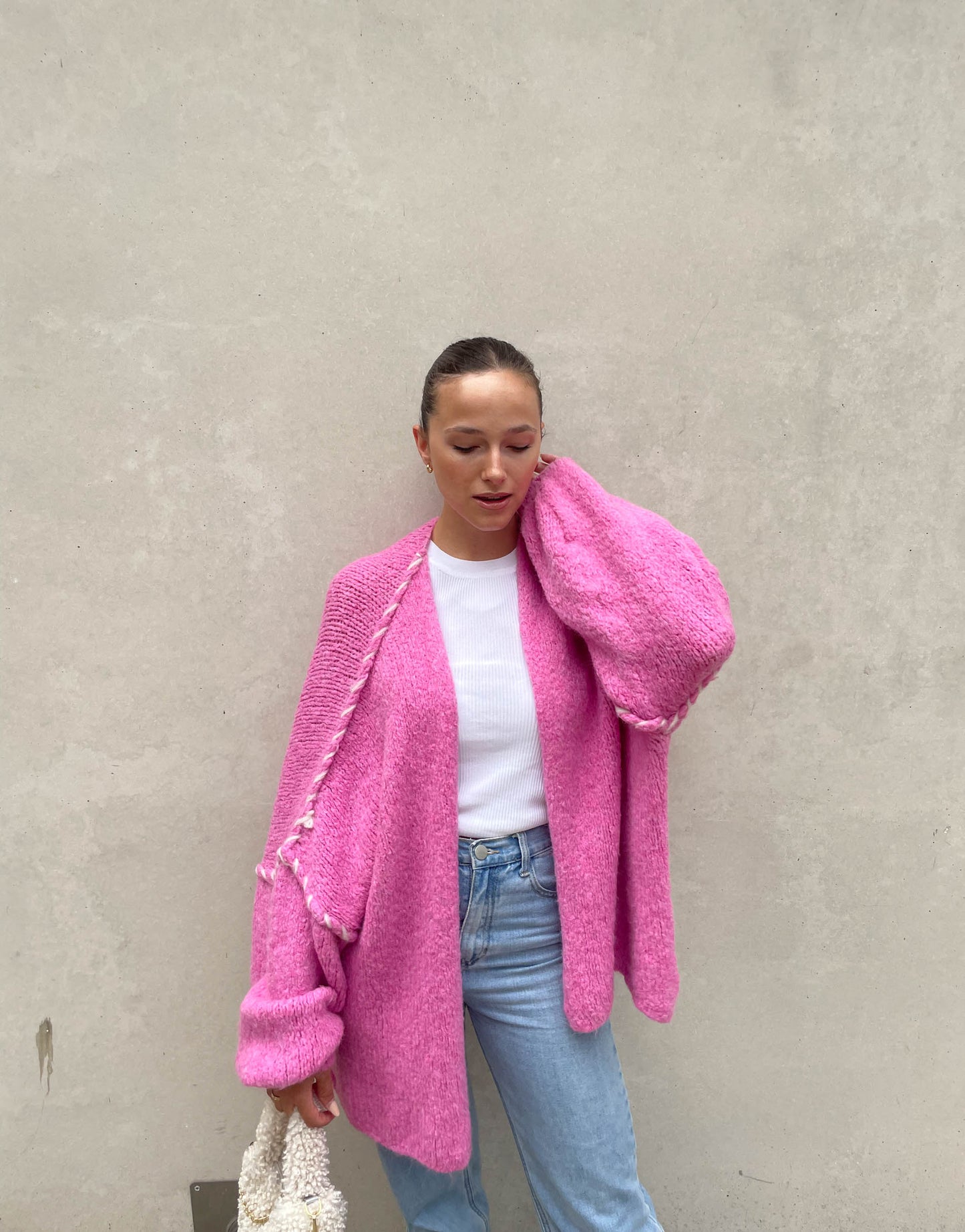 Frau mit brauen Haaren trägt Oversize Strickjacke mit farblich abgesetzter Aussennaht in pink