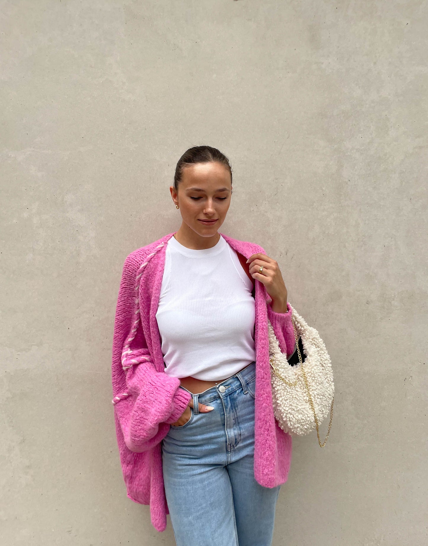 Frau mit brauen Haaren trägt Oversize Strickjacke mit farblich abgesetzter Aussennaht in pink