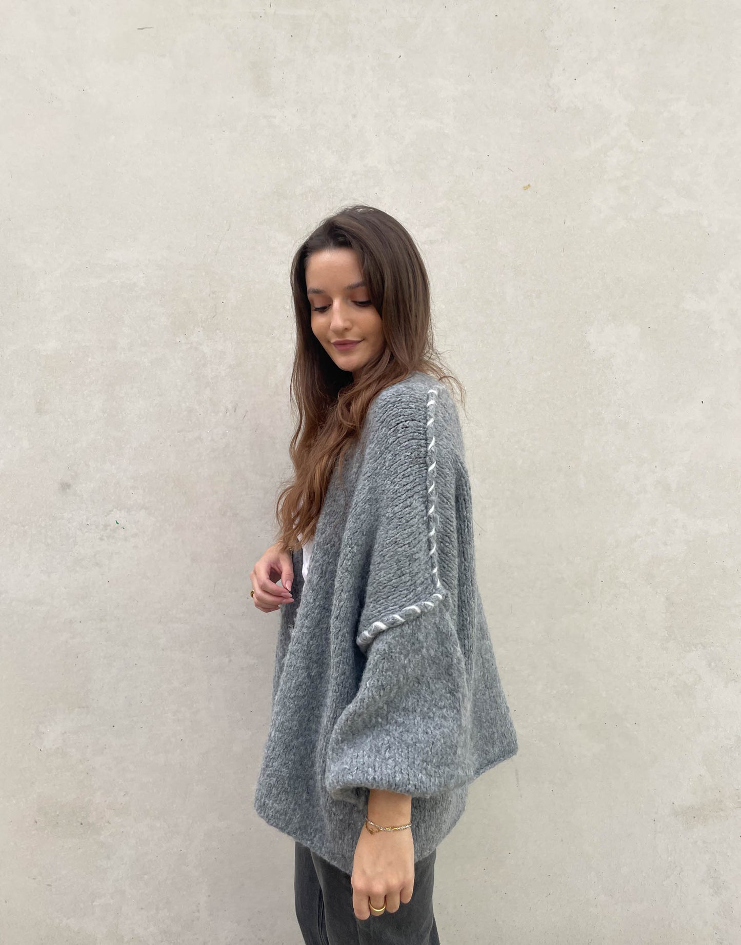 Frau mit brauen Haaren trägt Oversize Strickjacke mit farblich abgesetzter Aussennaht in grau