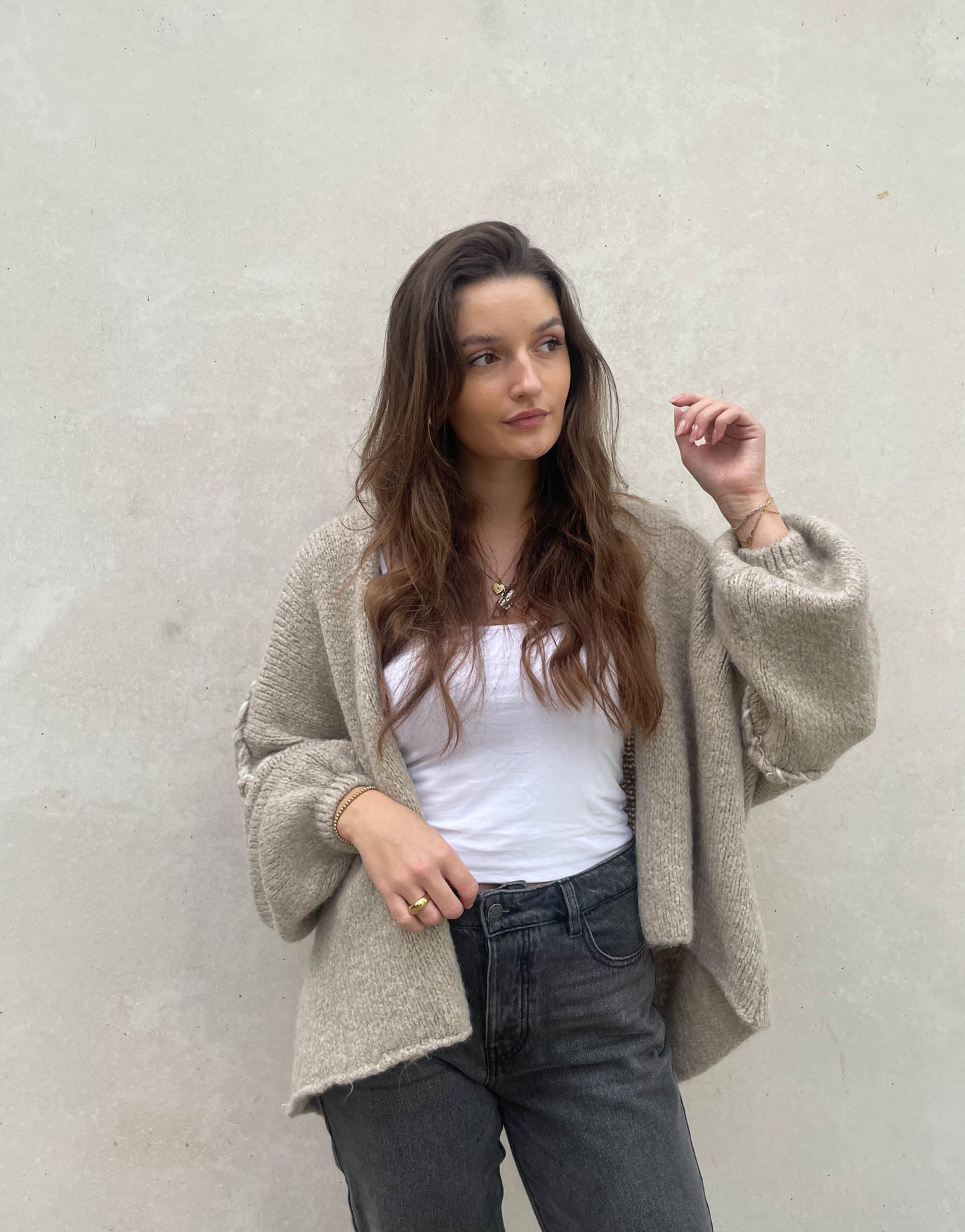 Frau mit brauen Haaren trägt Oversize Strickjacke mit farblich abgesetzter Aussennaht in beige