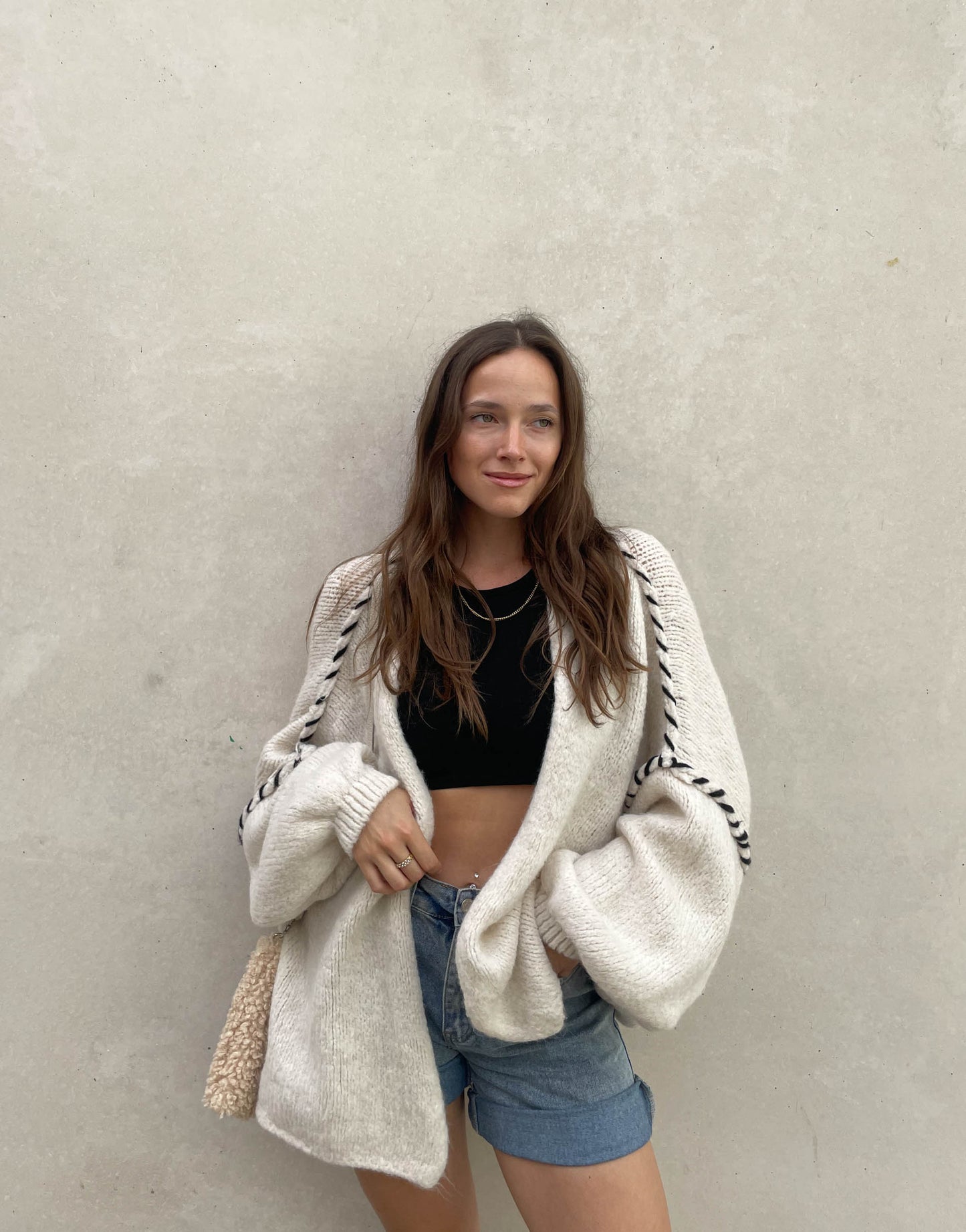 Frau mit brauen Haaren trägt Oversize Strickjacke mit farblich abgesetzter Aussennaht in beige