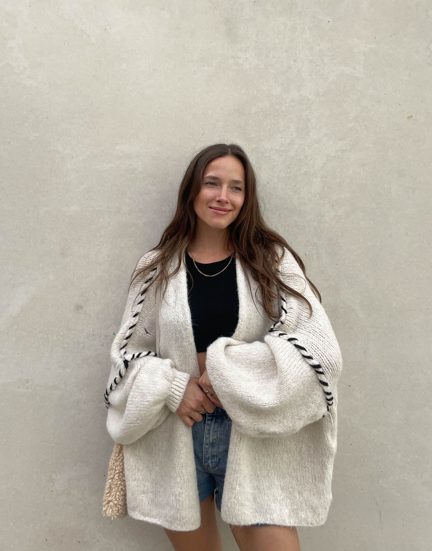 Frau mit brauen Haaren trägt Oversize Strickjacke mit farblich abgesetzter Aussennaht in beige