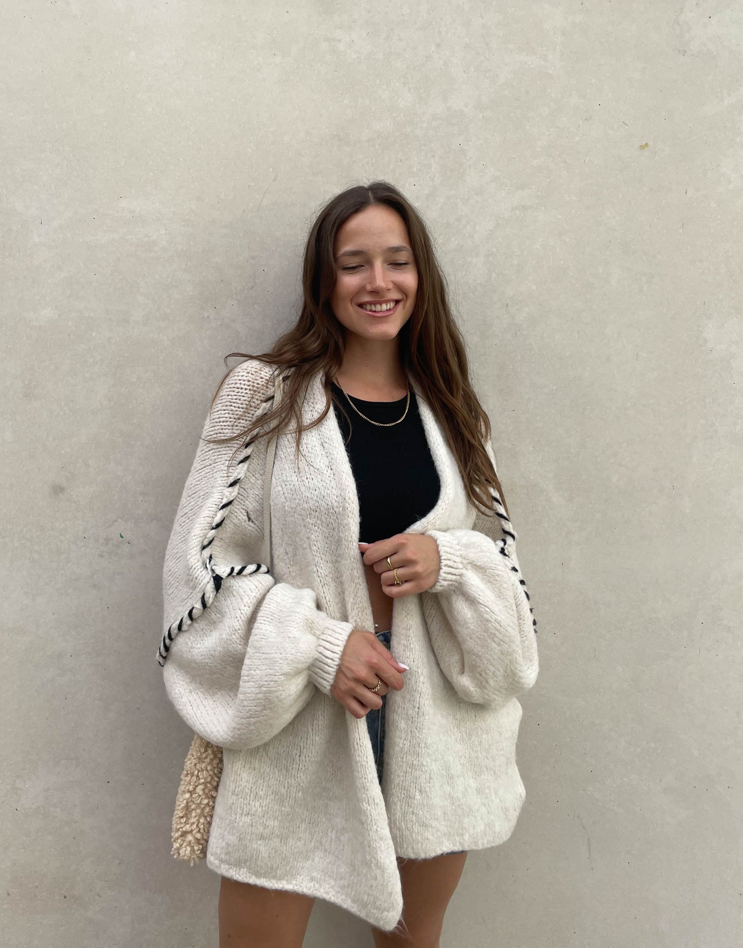 Frau mit brauen Haaren trägt Oversize Strickjacke mit farblich abgesetzter Aussennaht in beige