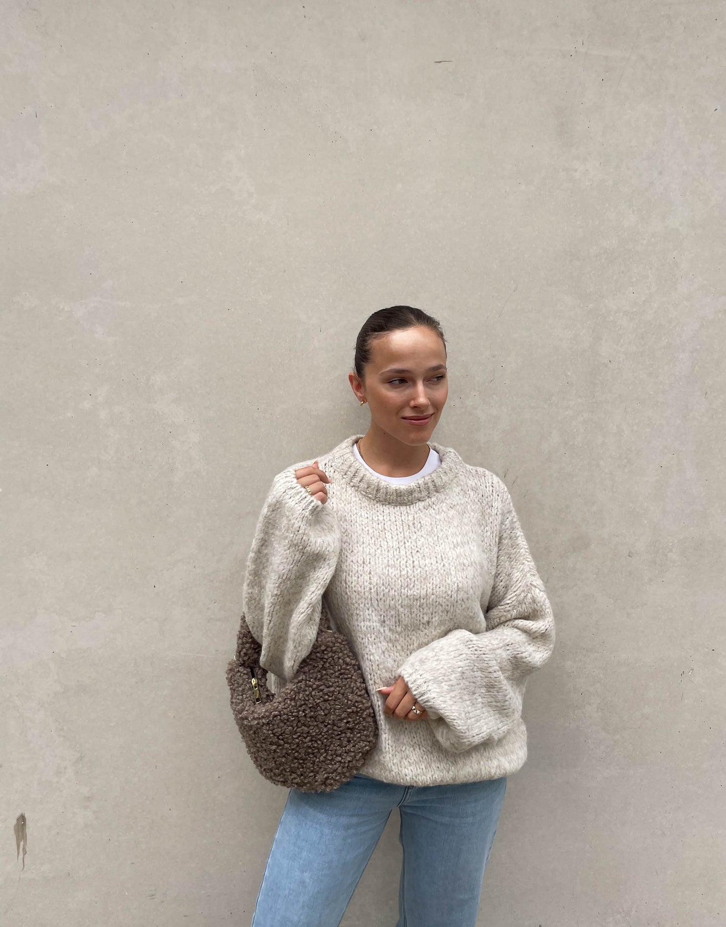 Frau mit brauen Haaren trägt weiten Strickpullover in Beige