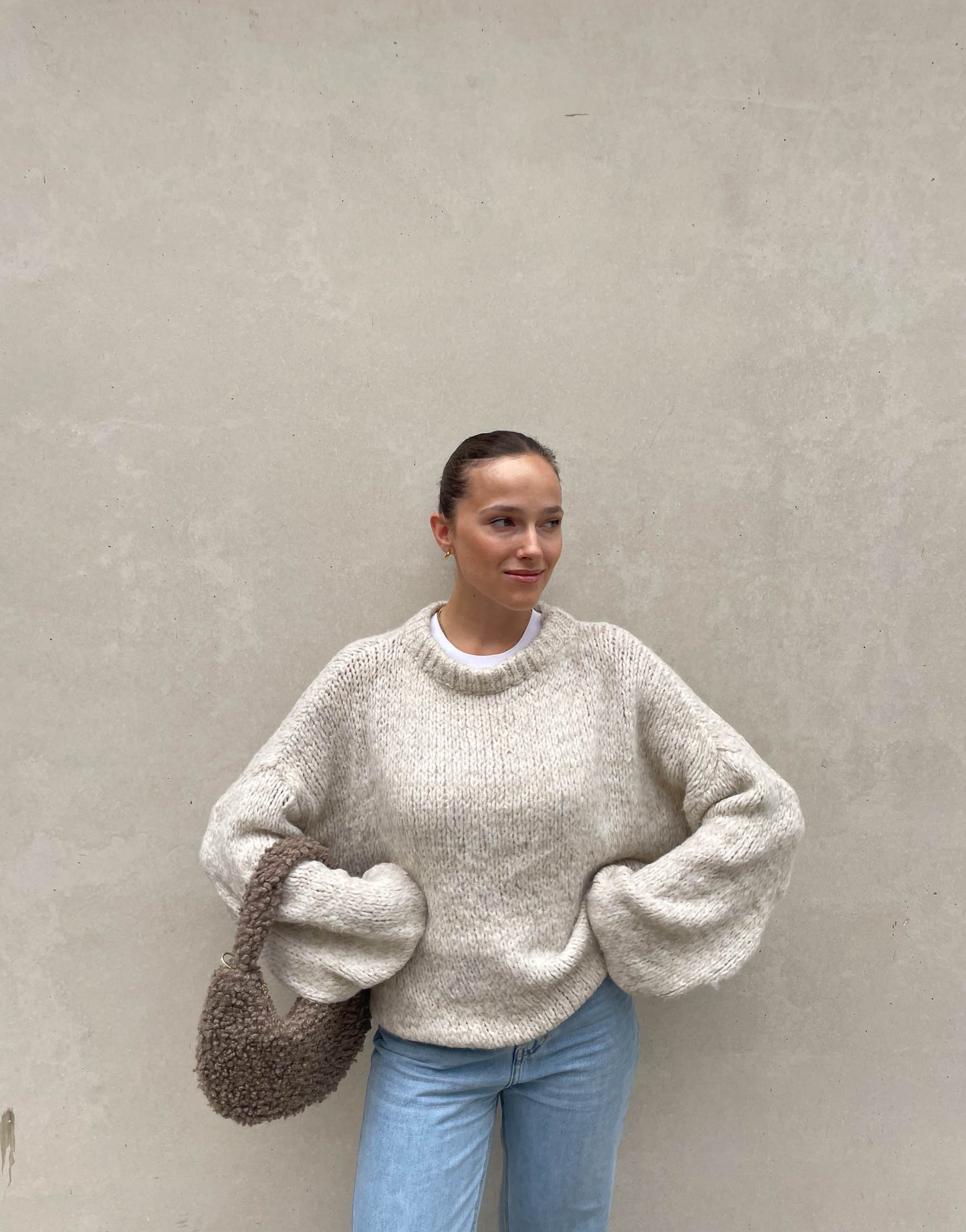 Frau mit brauen Haaren trägt weiten Strickpullover in Beige