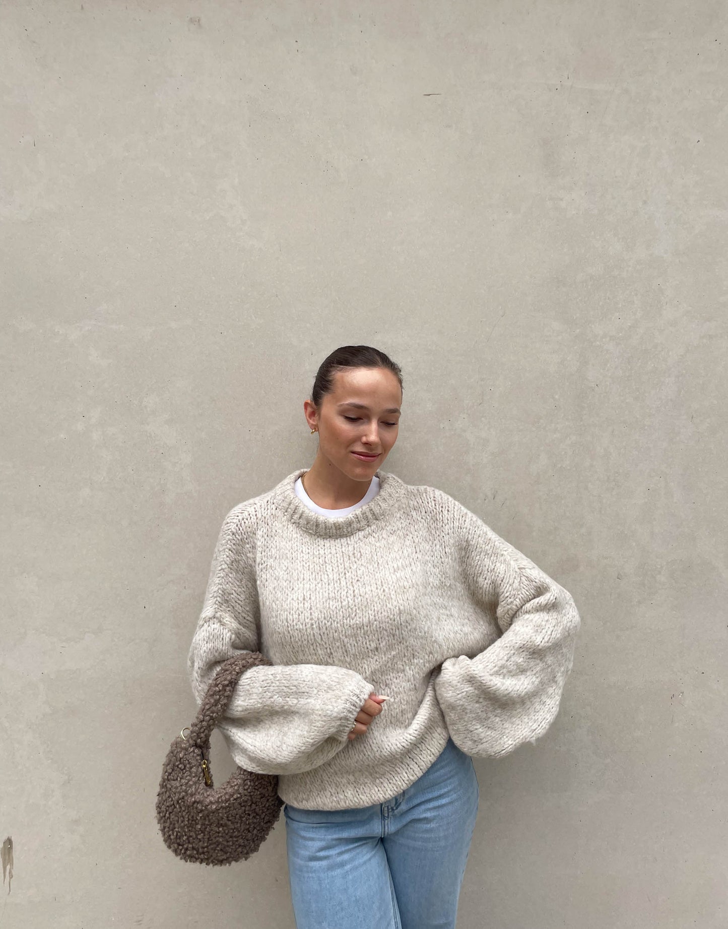 Frau mit brauen Haaren trägt weiten Strickpullover in Beige