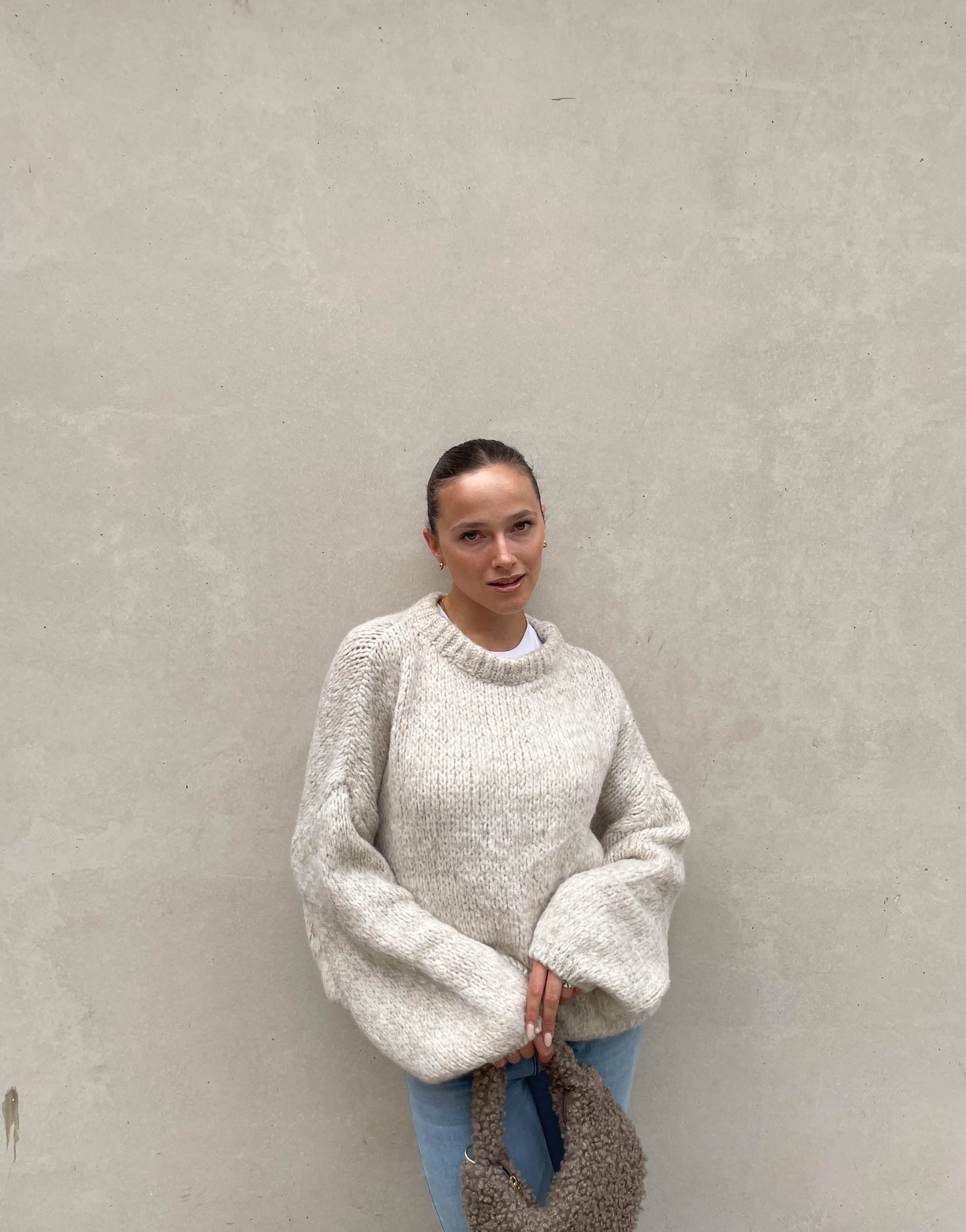 Frau mit brauen Haaren trägt weiten Strickpullover in Beige