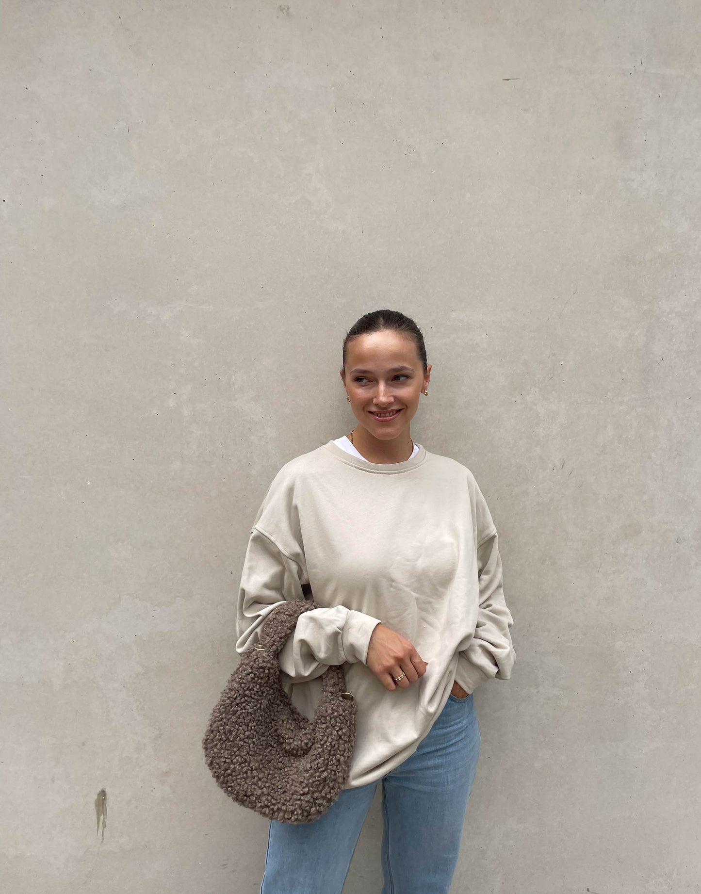 Frau mit brauen Haaren trägt Boucle Tasche in Taupe