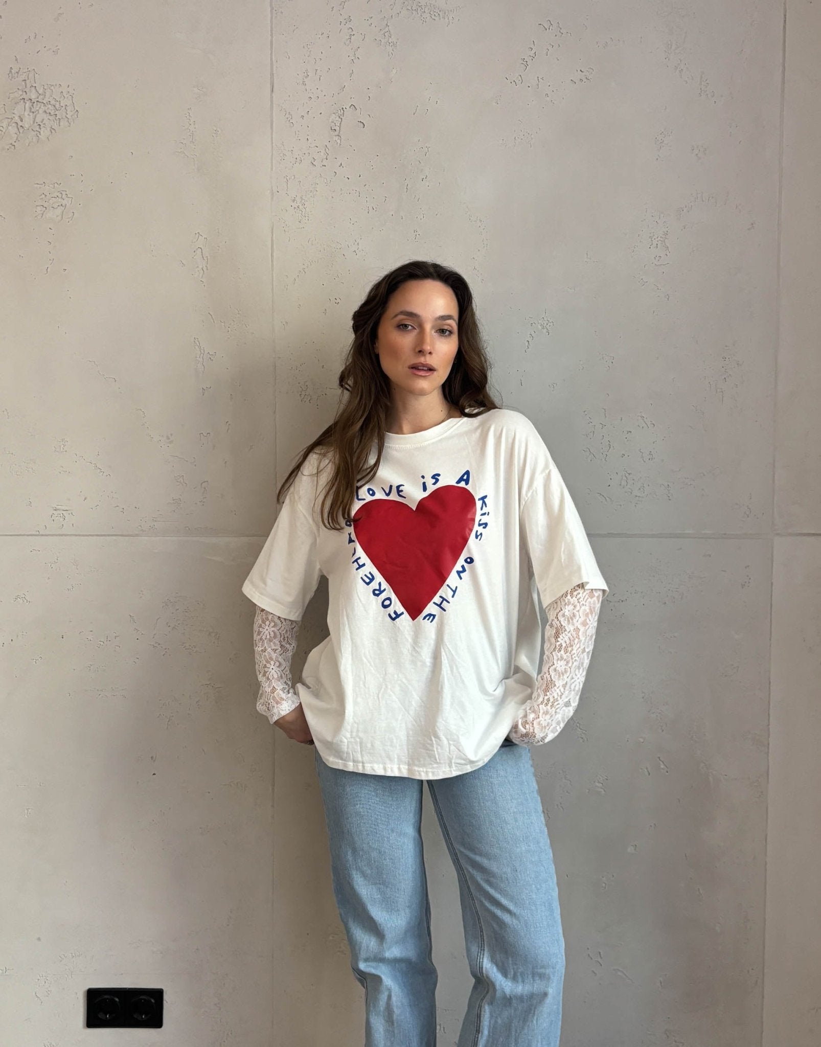 Frau mit braunen Haaren trägt weißes T-Shirt mit Print und Spitzeneinsatz am Arm