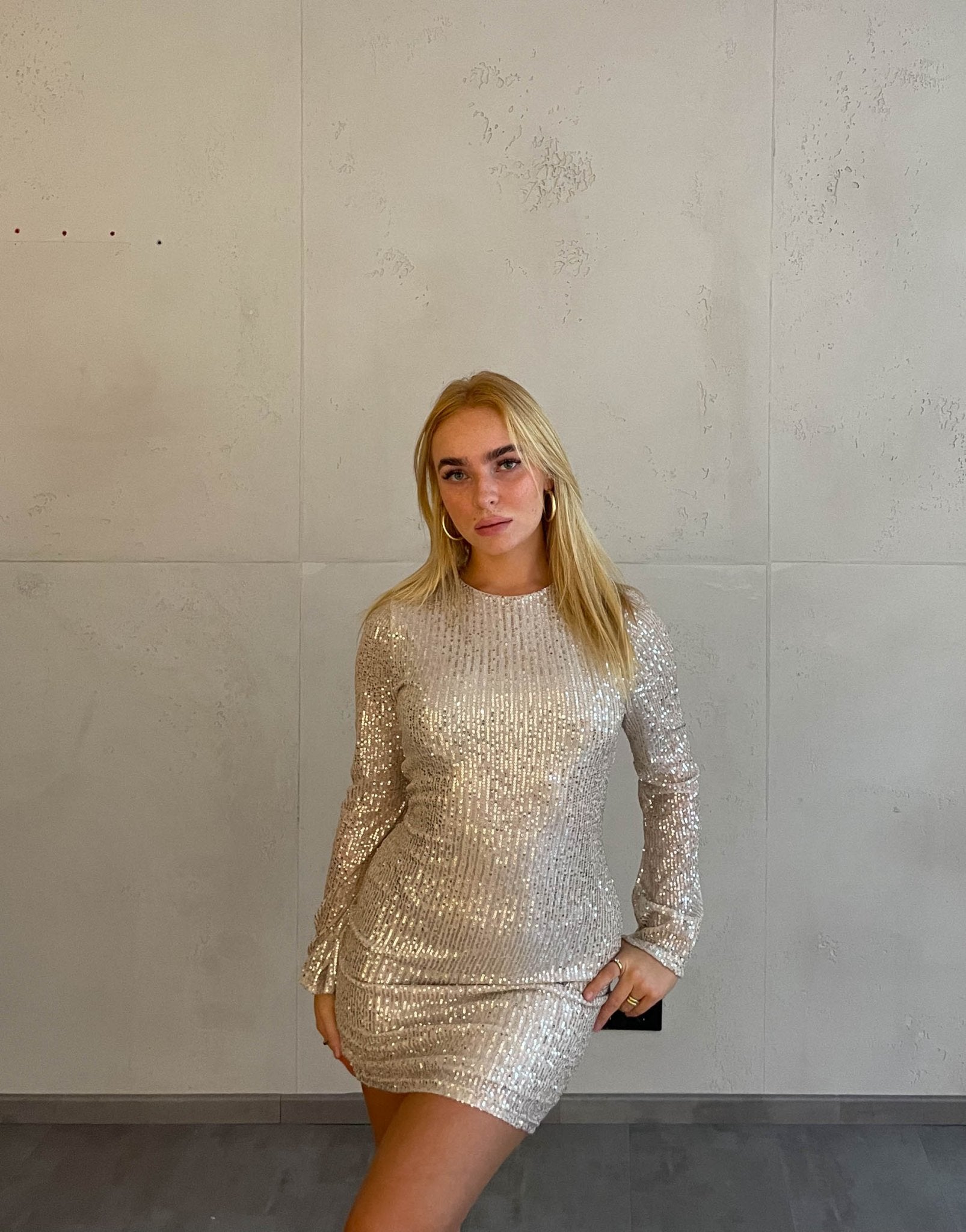 Frau mit blonden Haaren trägt kurzes Paillettenkleid in Gold