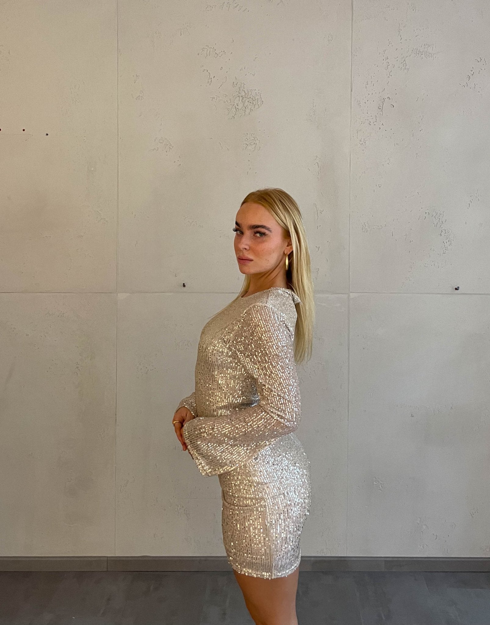 Frau mit blonden Haaren trägt kurzes Paillettenkleid in Gold