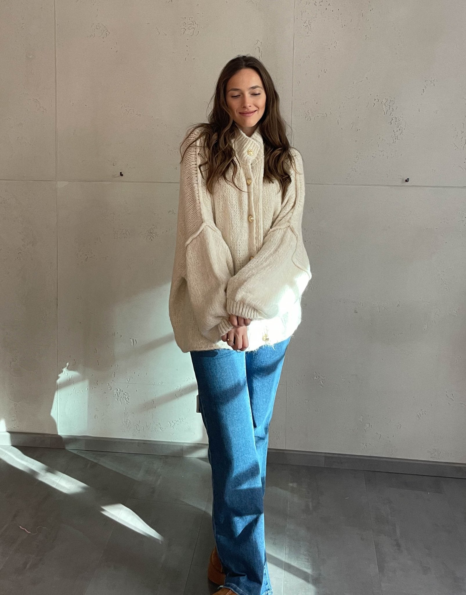 Frau mit brauen Haaren trägt oversize Strickjacke in Hellbeige