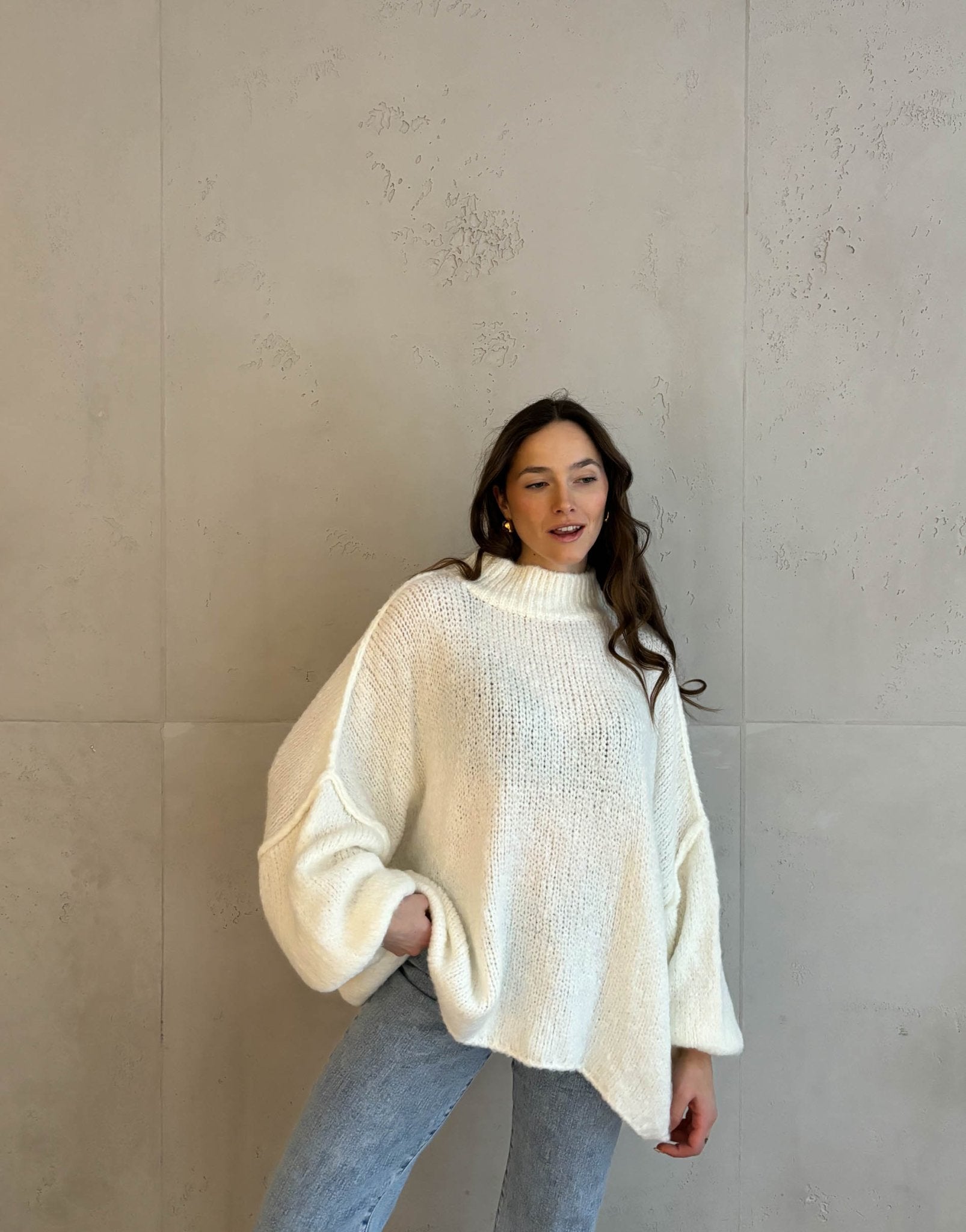 Frau mit brauen Haaren trägt oversize Strickpullover in wollweiß