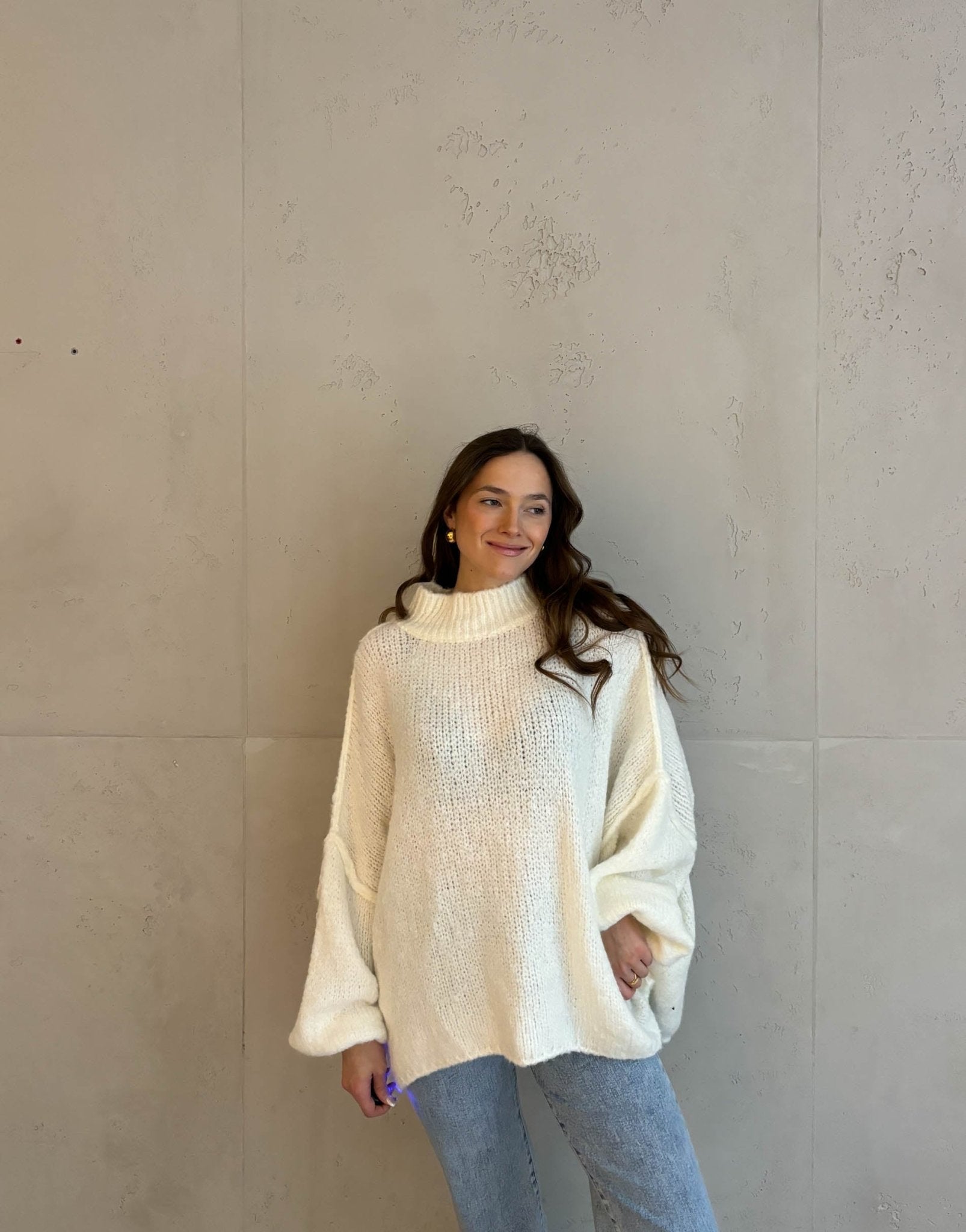 Frau mit brauen Haaren trägt oversize Strickpullover in wollweiß