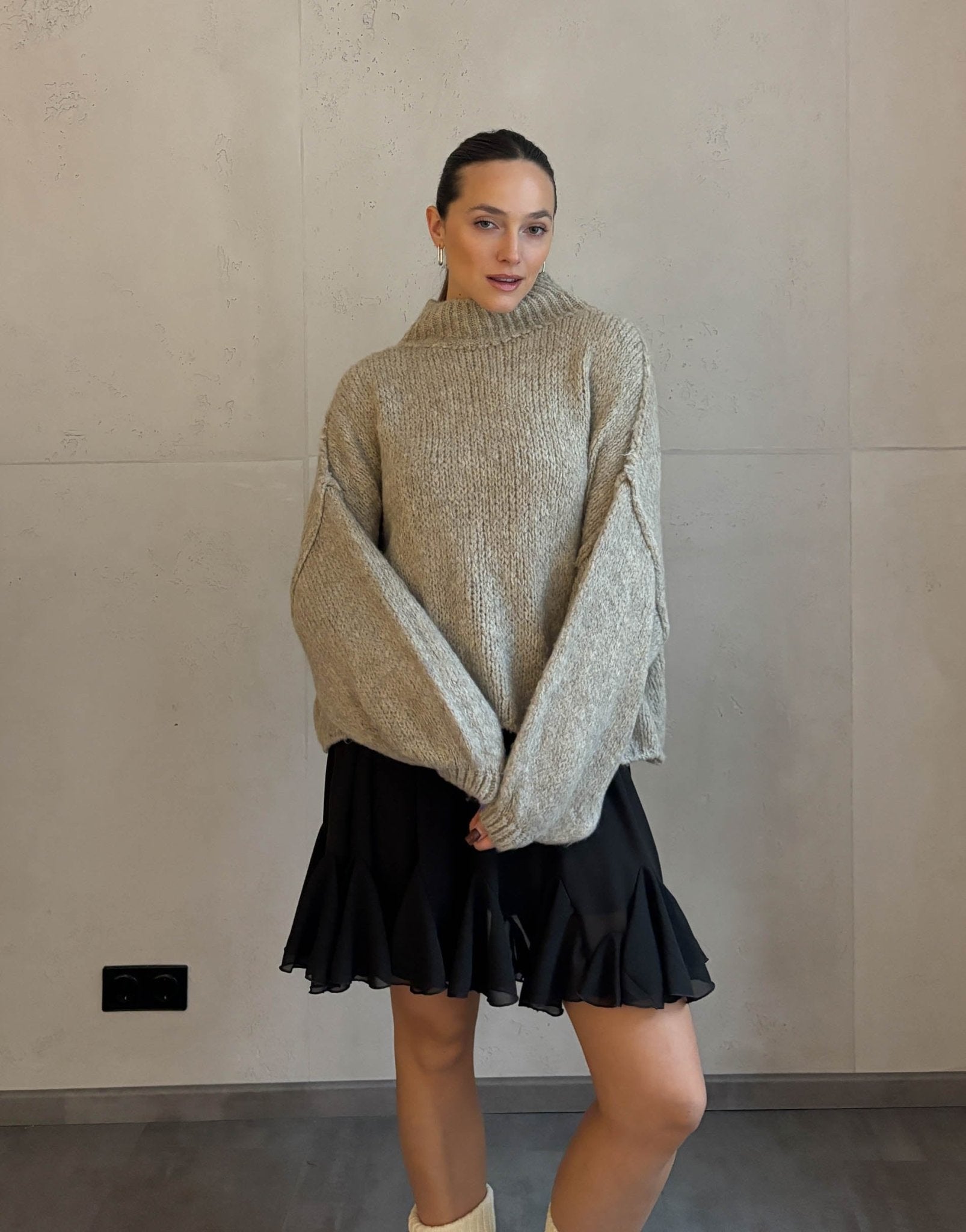 Frau mit braunen Haaren trägt kurzen oversize Pullover mit Stehkragen in taupe