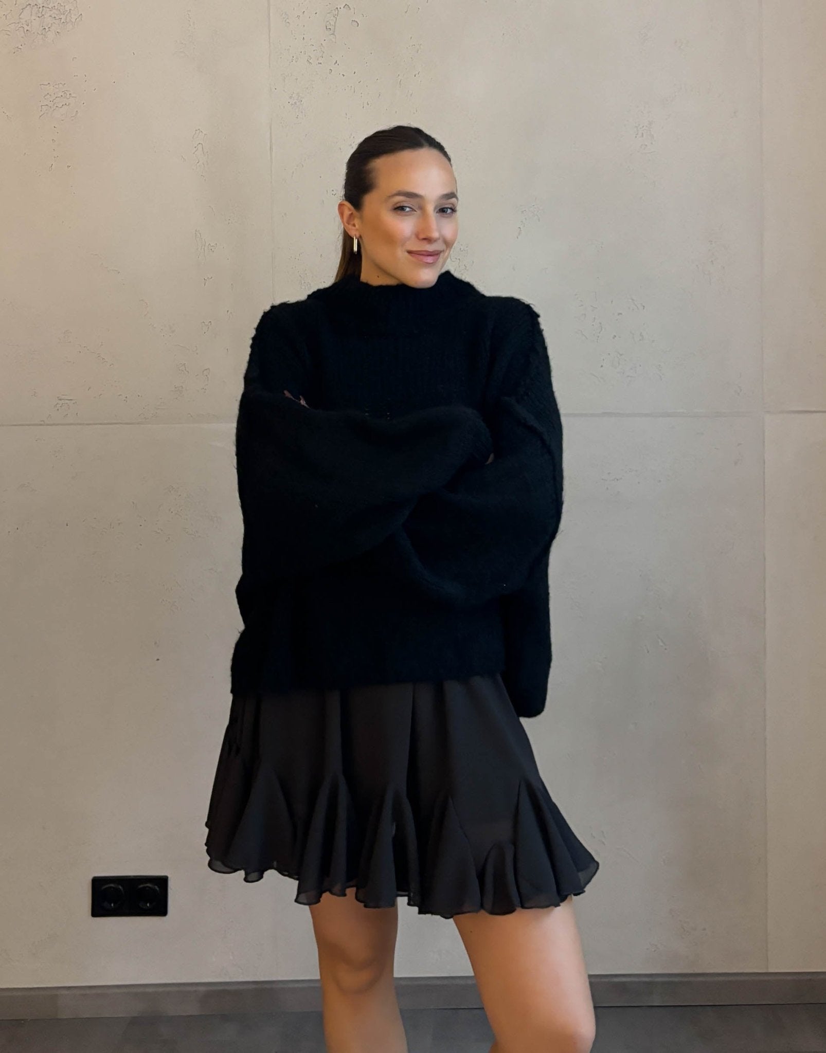 Frau mit braunen Haaren trägt kurzen oversize Pullover mit Stehkragen in schwarz