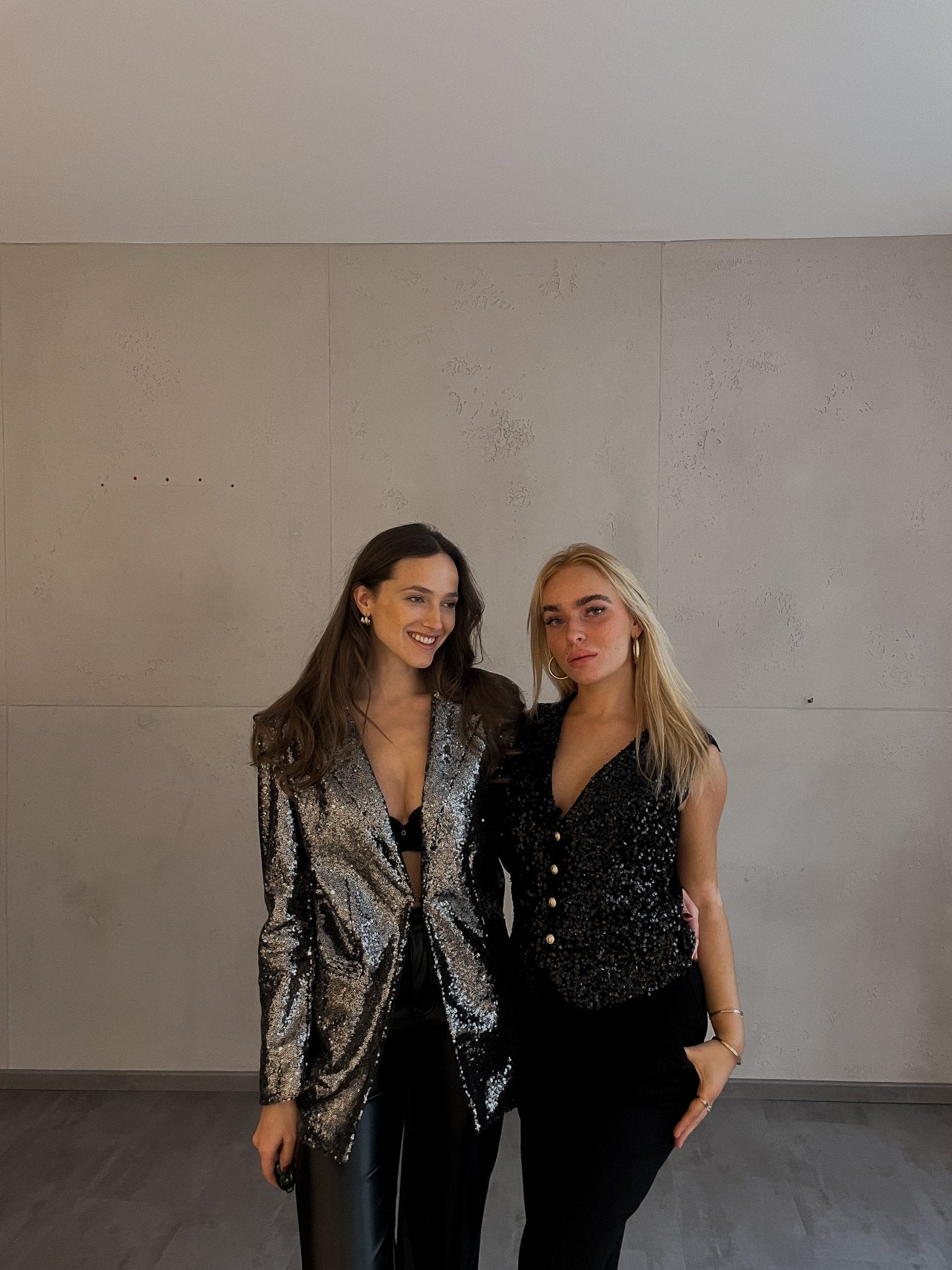 Frau mit brauen Haaren trägt Glitzerblazer und Frau mit blonden Haaren eine glitzerweste