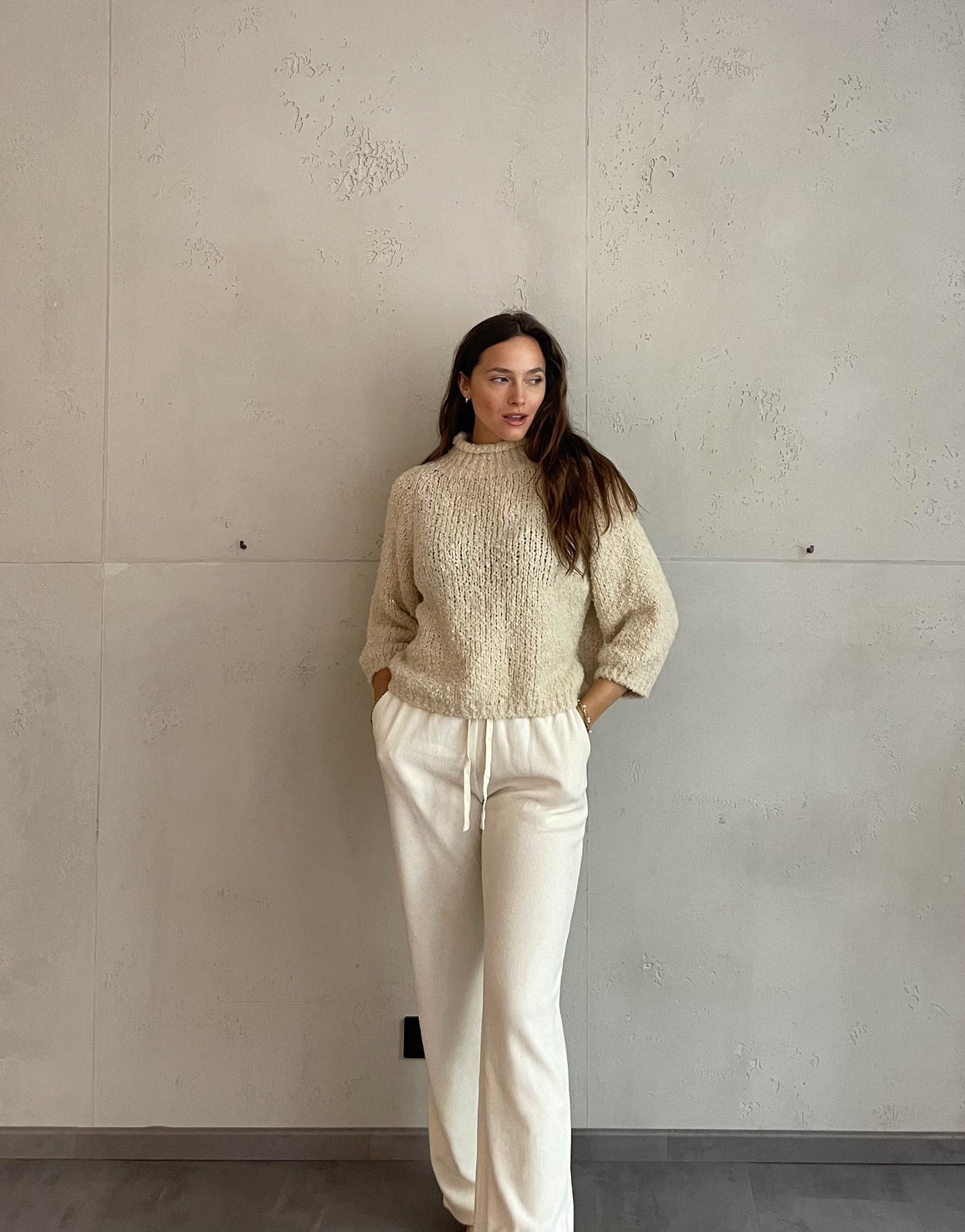 Frau mit brauen Haaren trägt Boucle Pulli mit Stehkragen in Beige