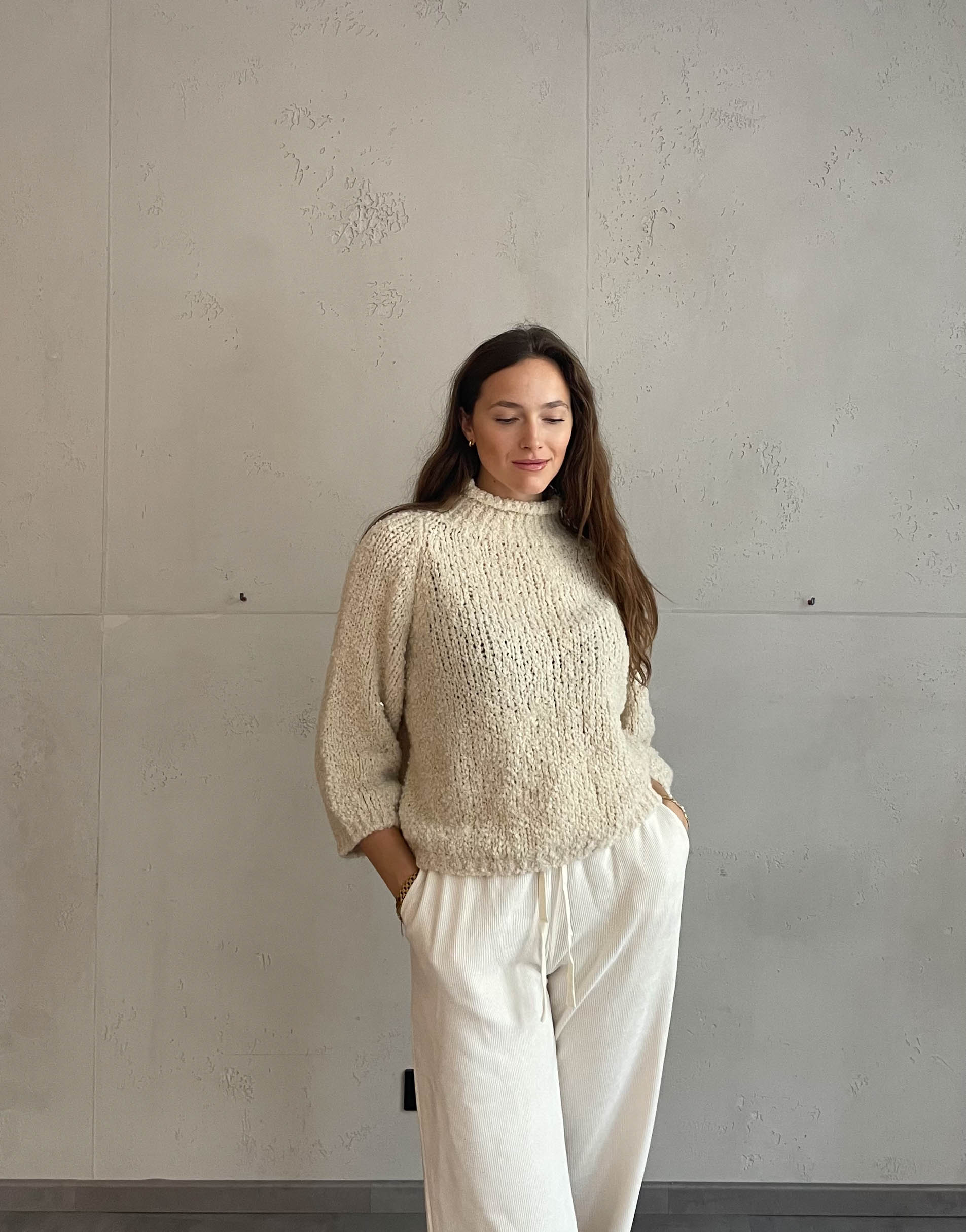 Frau mit brauen Haaren trägt Boucle Pulli mit Stehkragen in Beige