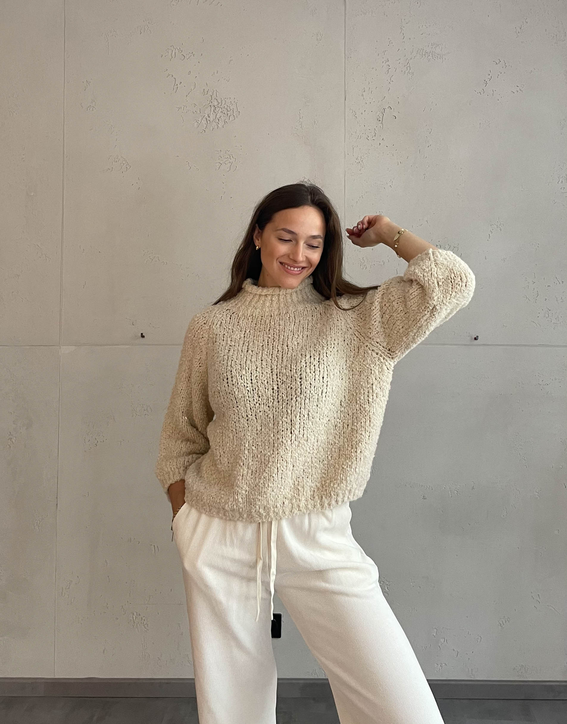 Frau mit brauen Haaren trägt Boucle Pulli mit Stehkragen in Beige