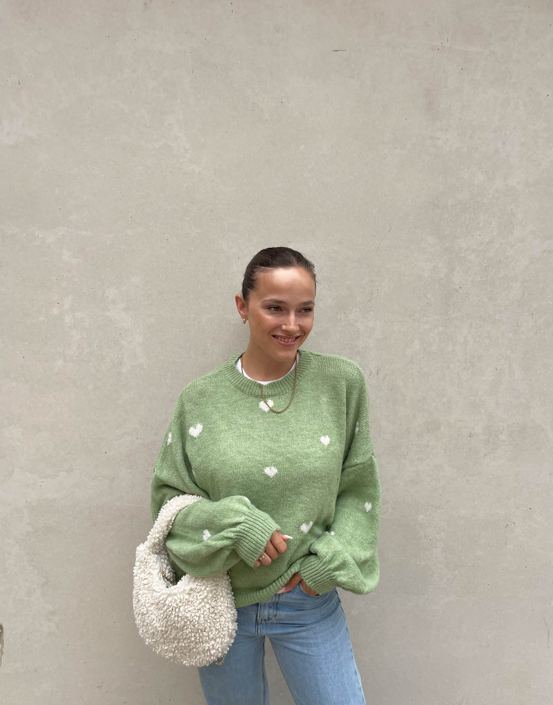 Frau mit brauen Haaren trägt Pullover mit Herzchen in Mint