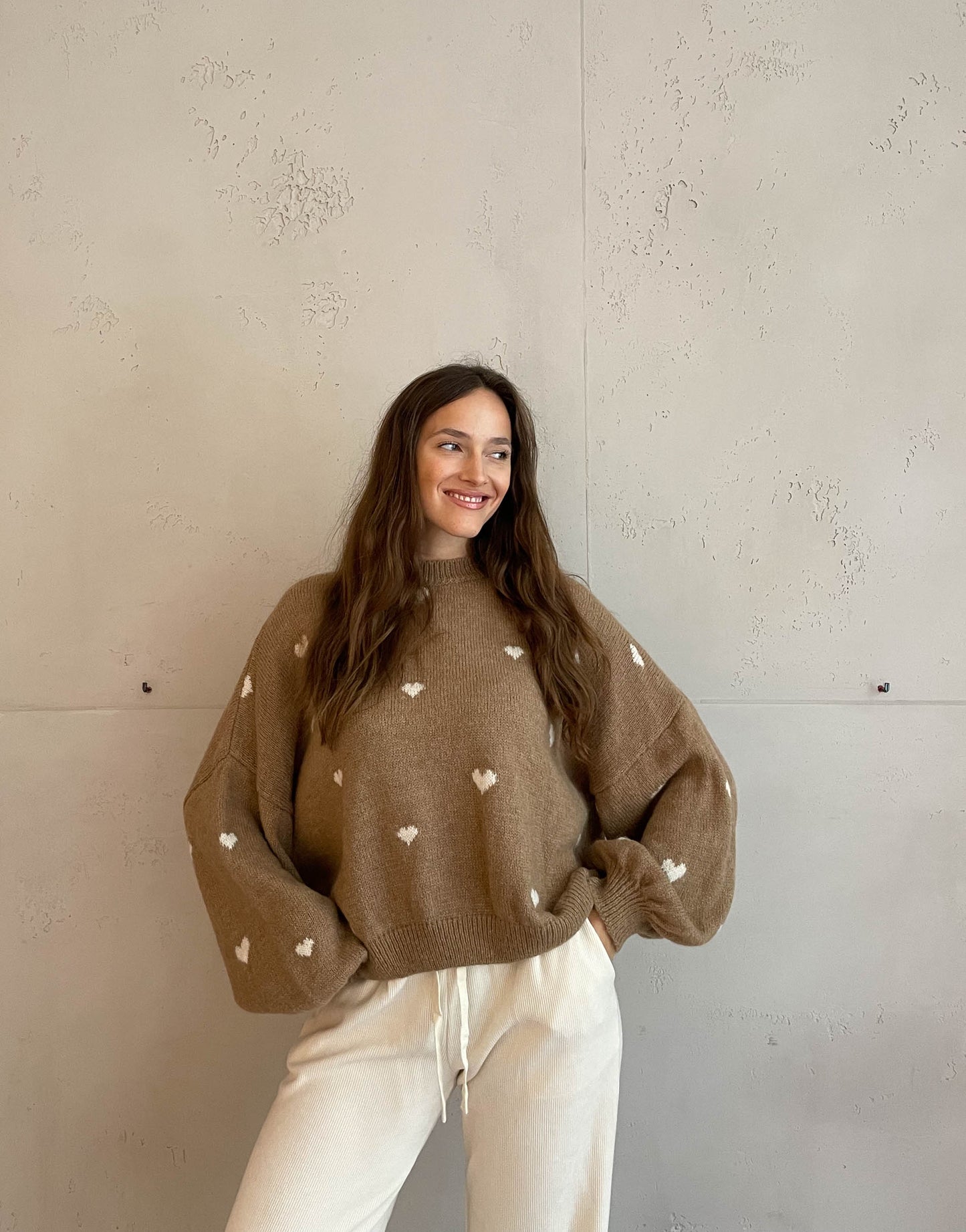 Frau mit brauen Haaren trägt Herzpullover in camel