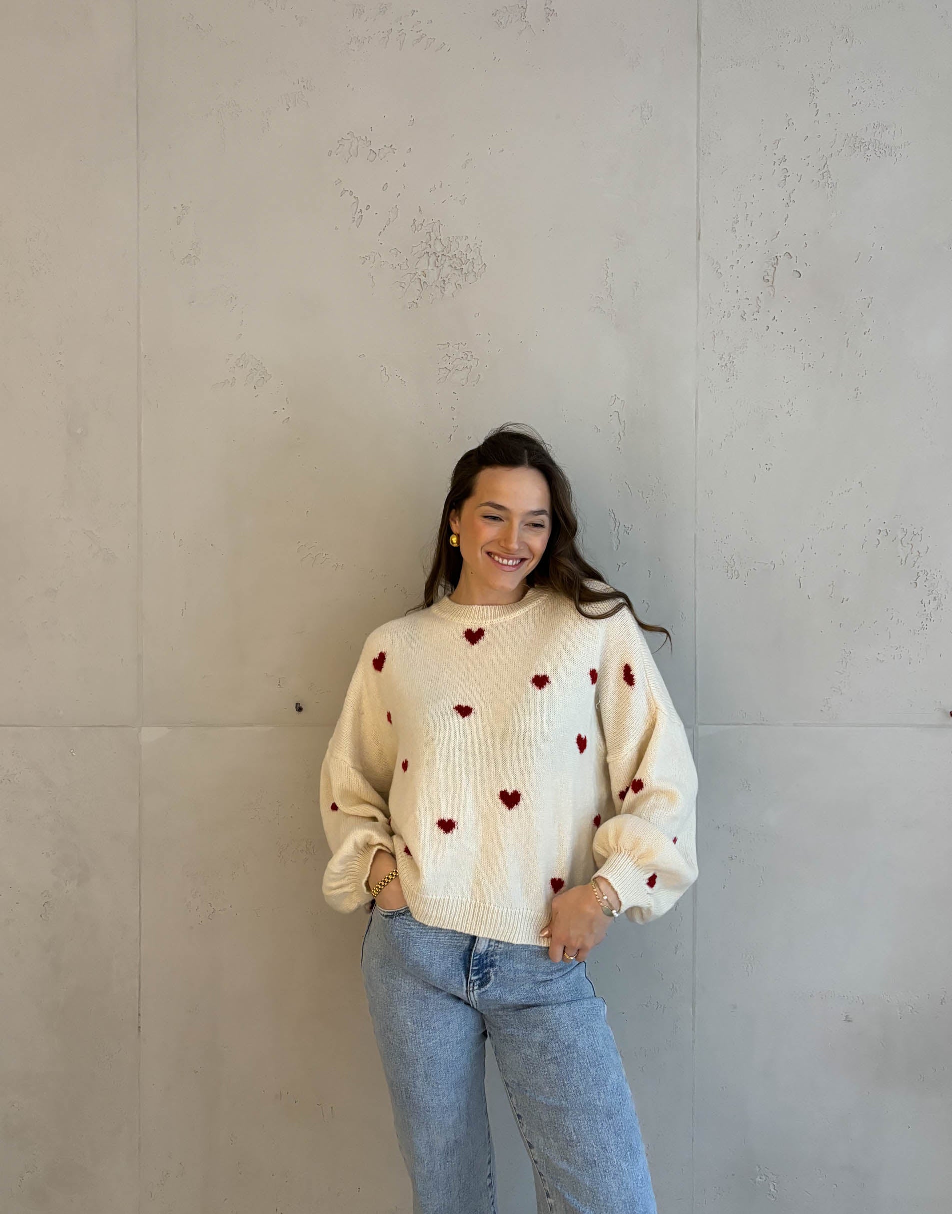 Frau mit brauen Haaren trägt Herzpullover in Beige mit roten Herzen