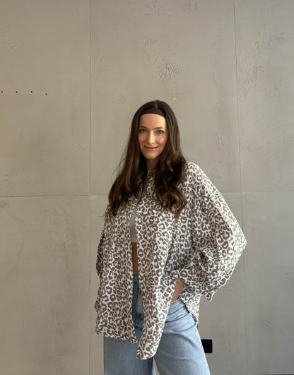 Frau mit brauen Haaren trägt Musselinbluse mit Leoprint in beige