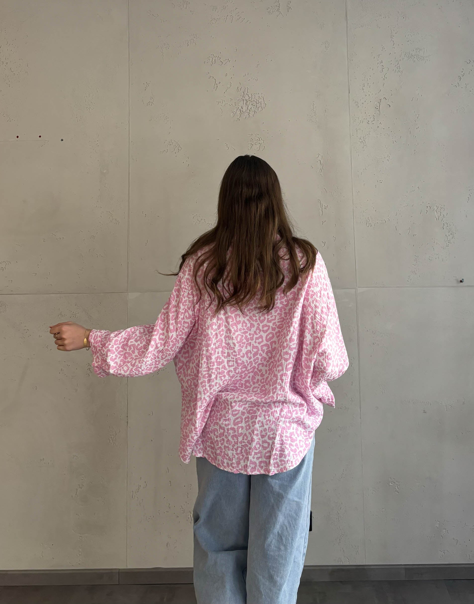 Frau mit brauen Haaren trägt Musselinbluse mit Leoprint in rosa
