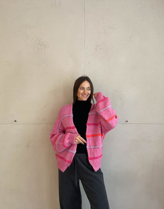 Frau mit brauen Haaren trägt Strickjacke mit Neon Aussennähten in Pink