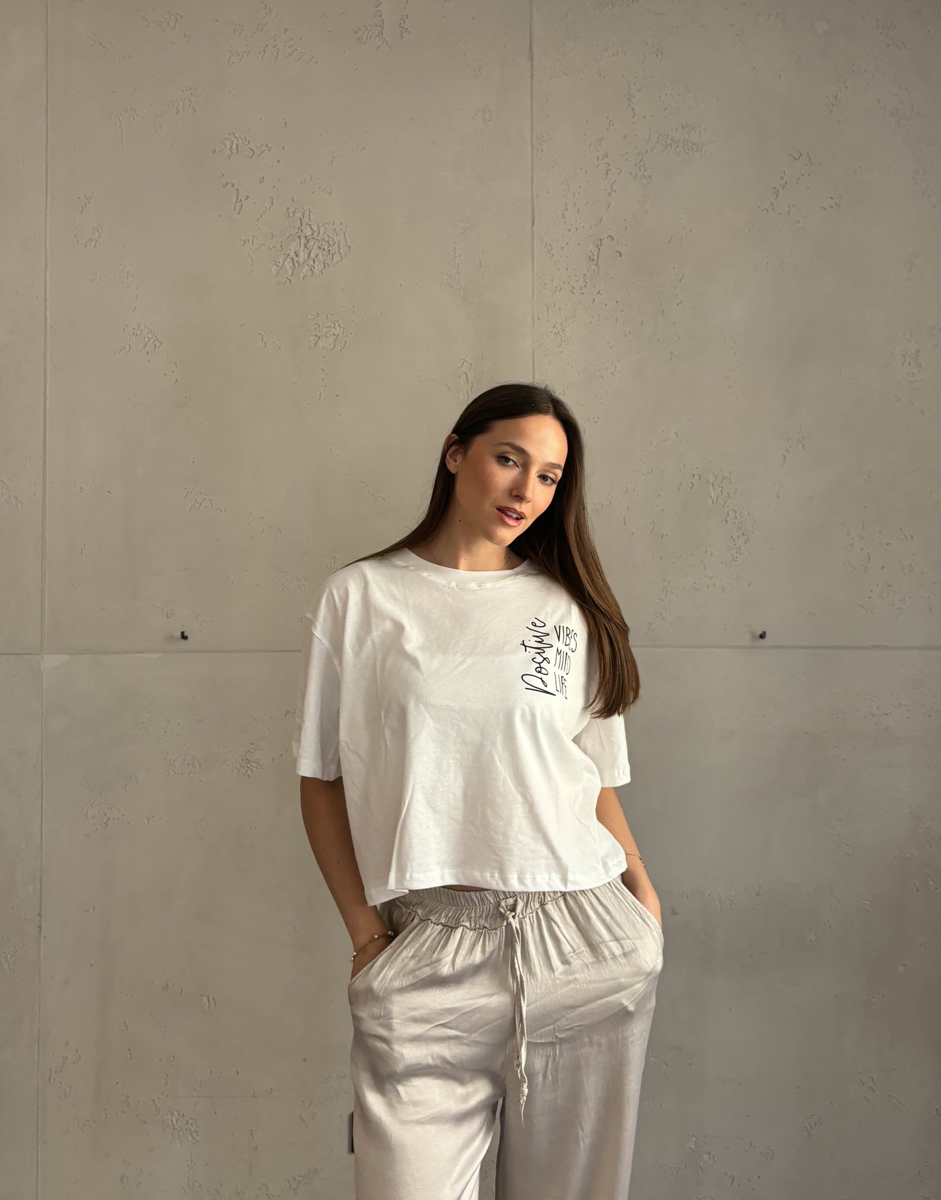 Frau mit braunen Haaren trägt weißes T-Shirt mit Aufschrift: positive vibes, mind, life