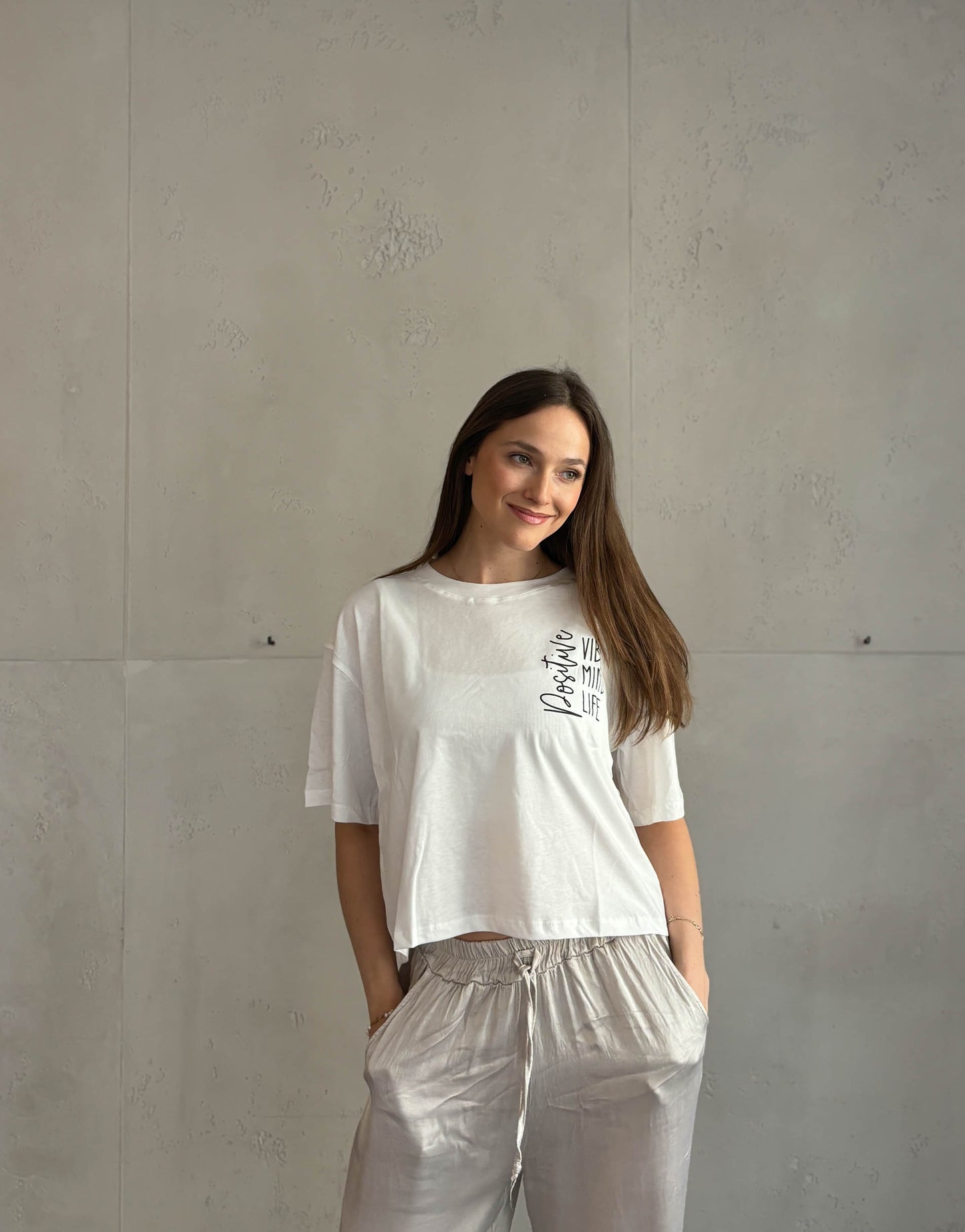 Frau mit braunen Haaren trägt weißes T-Shirt mit Aufschrift: positive vibes, mind, life